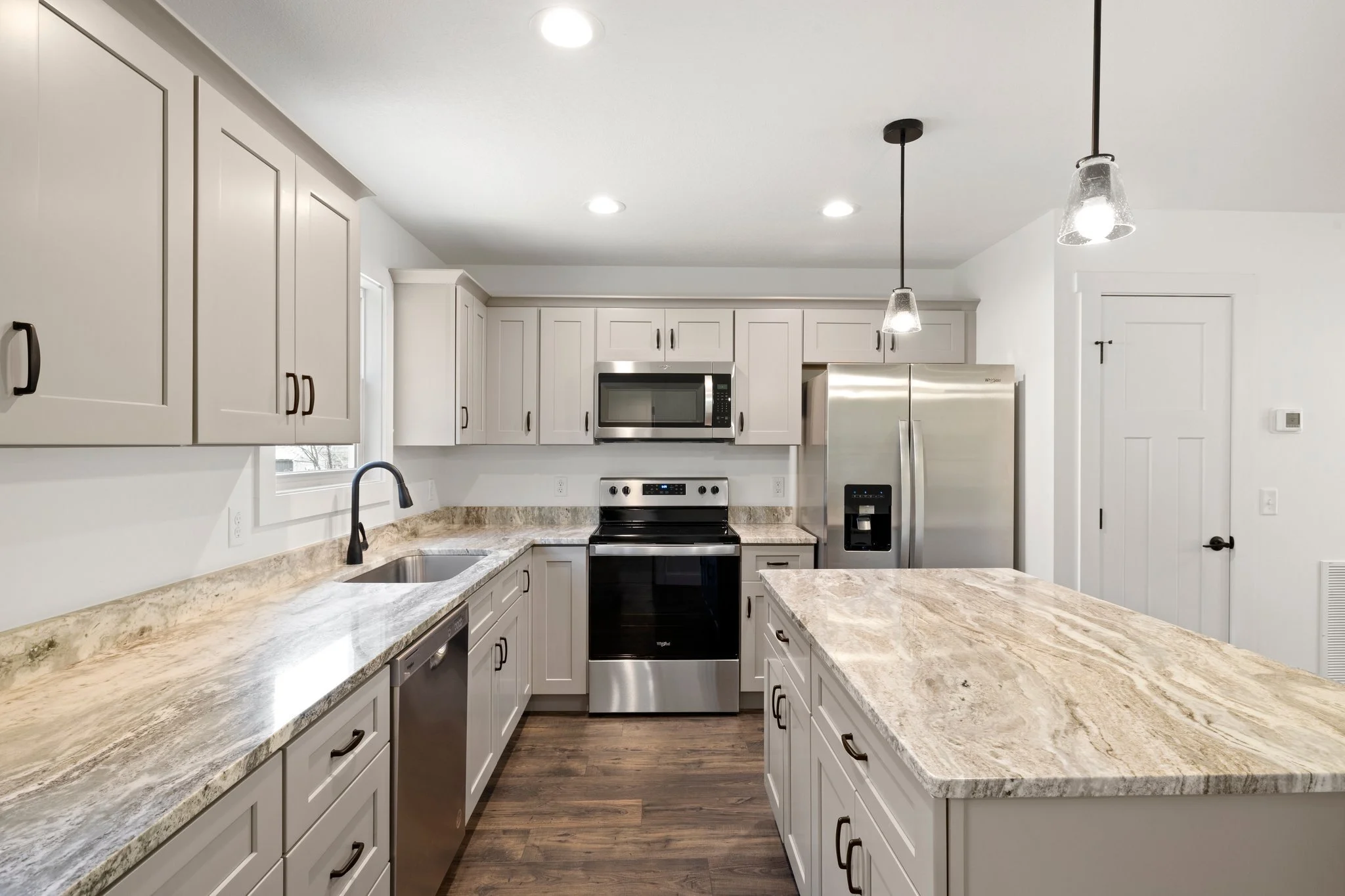 Modern kitchen with white cabinets, marble countertops, stainless steel appliances, and wood flooring.