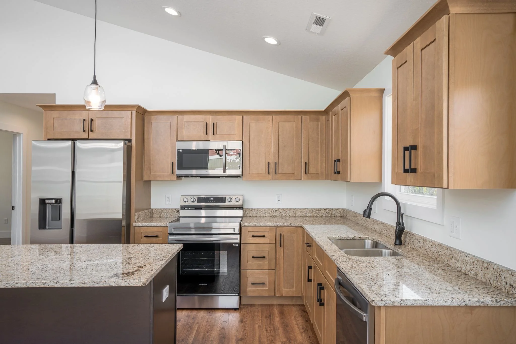 Modern kitchen with wooden cabinets, granite countertops, stainless steel appliances, and a double sink under a window.