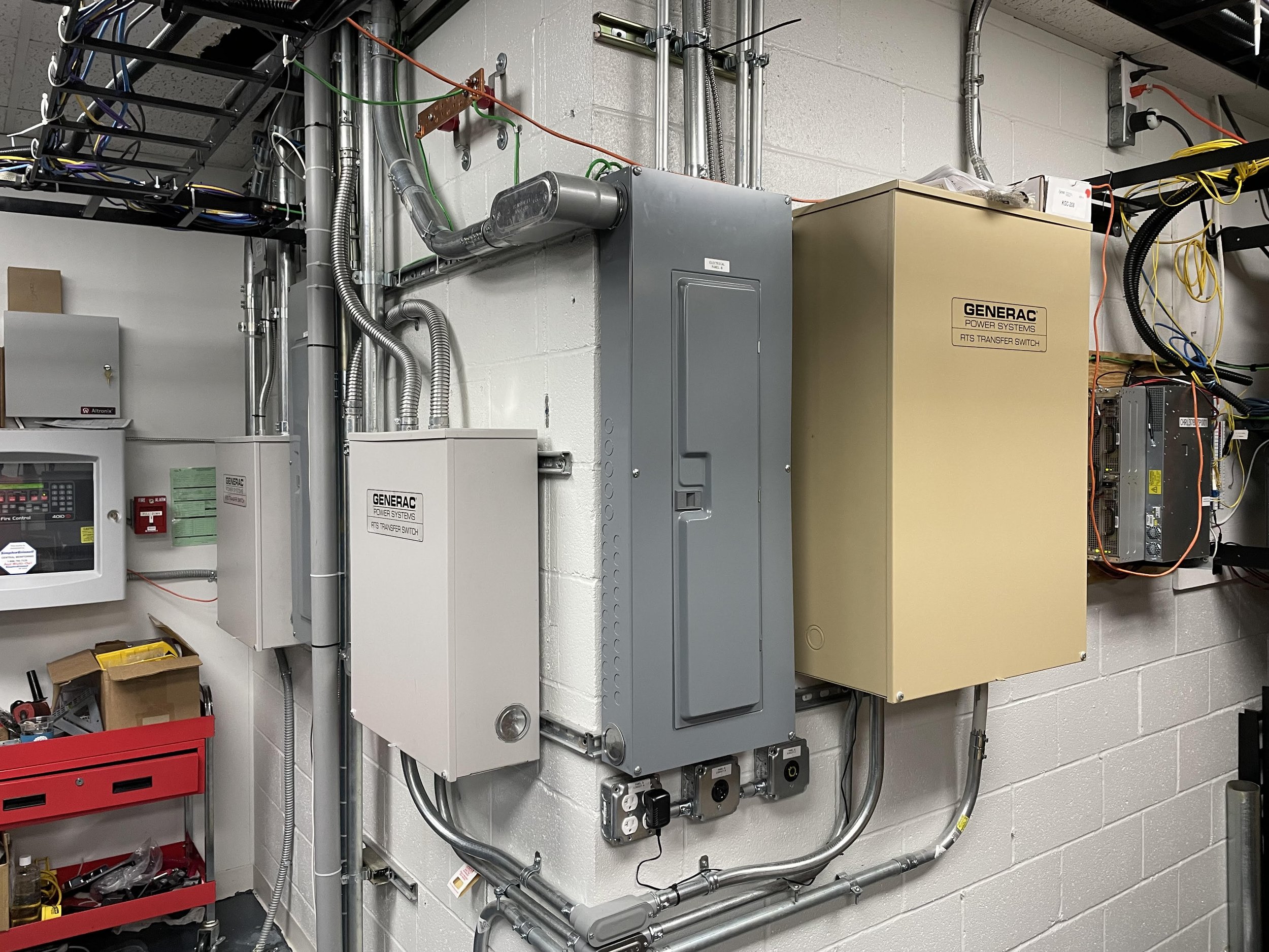 Electrical control panels and wiring mounted on a white brick wall in an industrial setting.