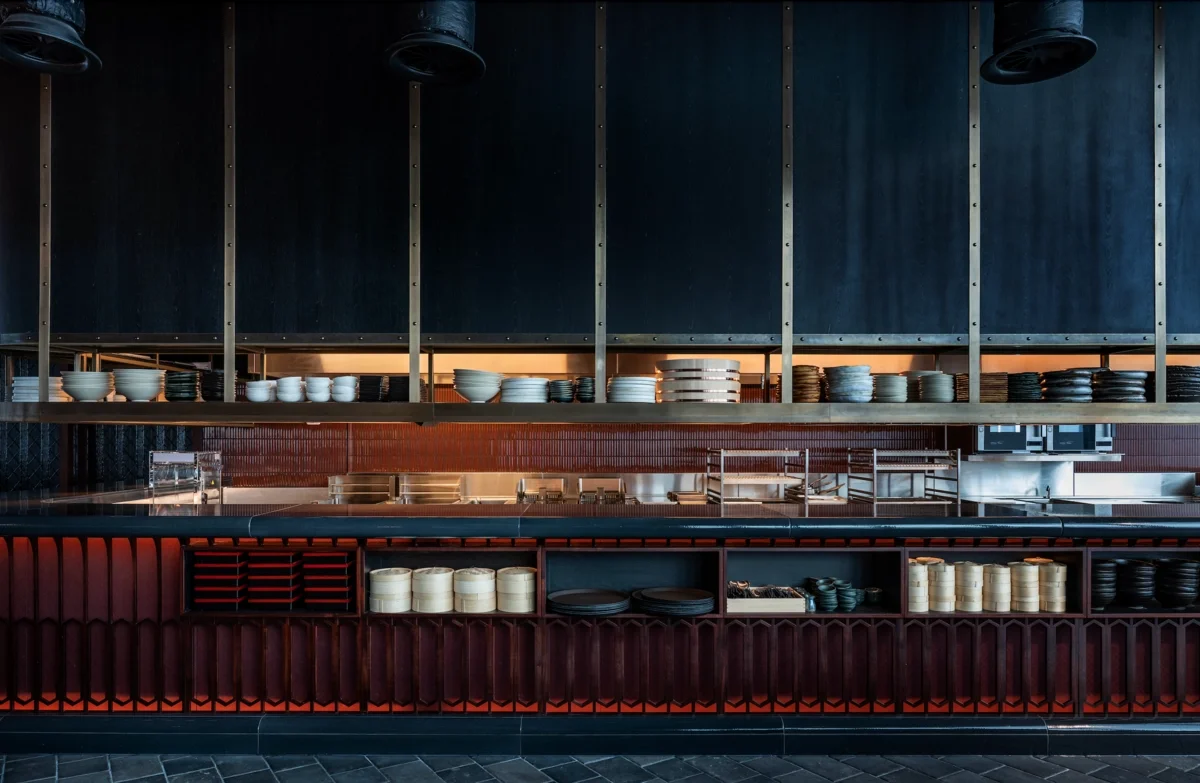 Interior of a modern restaurant kitchen with shelves of plates, bowls, and dishes, and a counter with some utensils and black cookware.