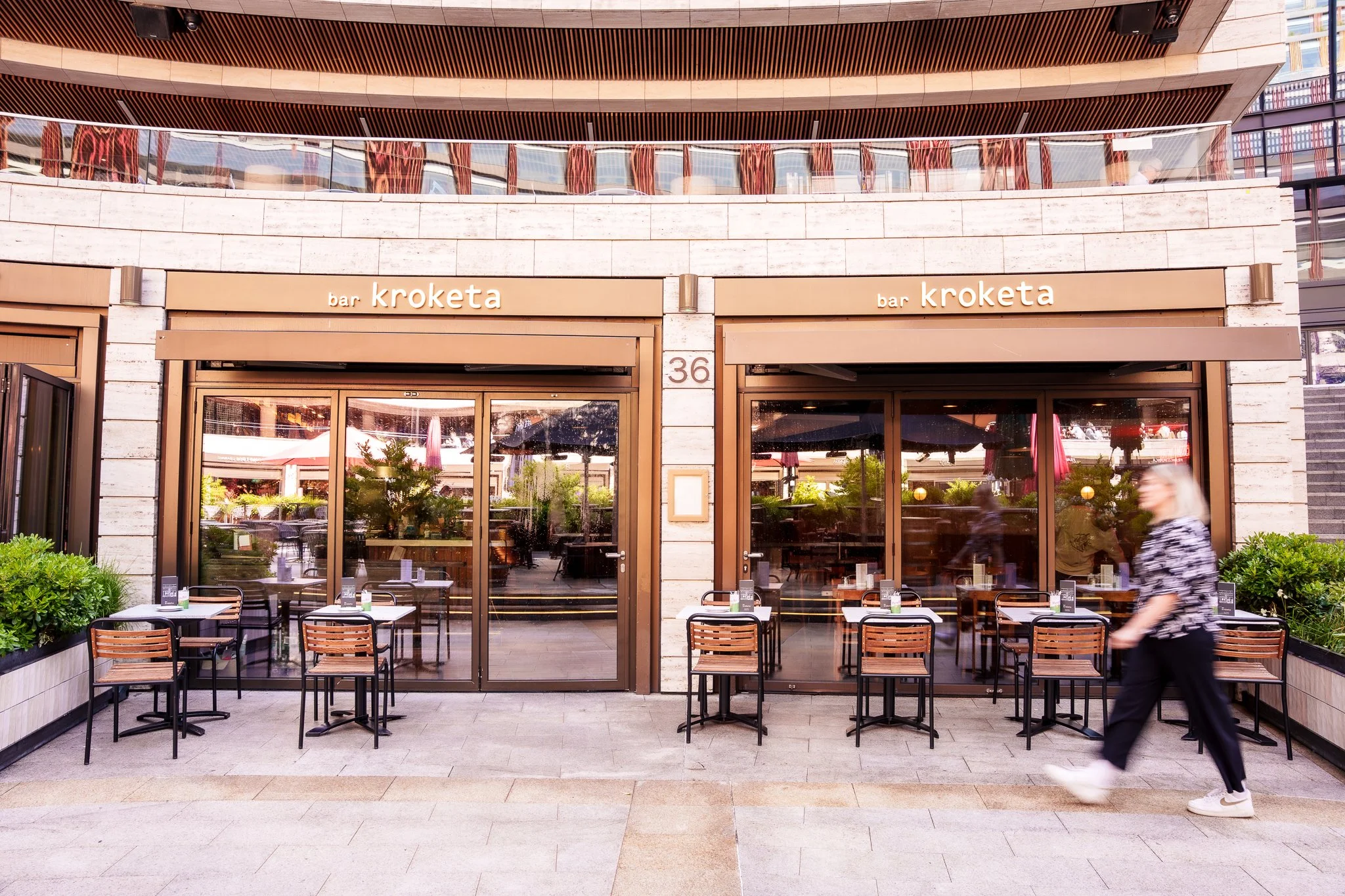 Exterior of bar Kroketta with outdoor seating and a woman walking past.