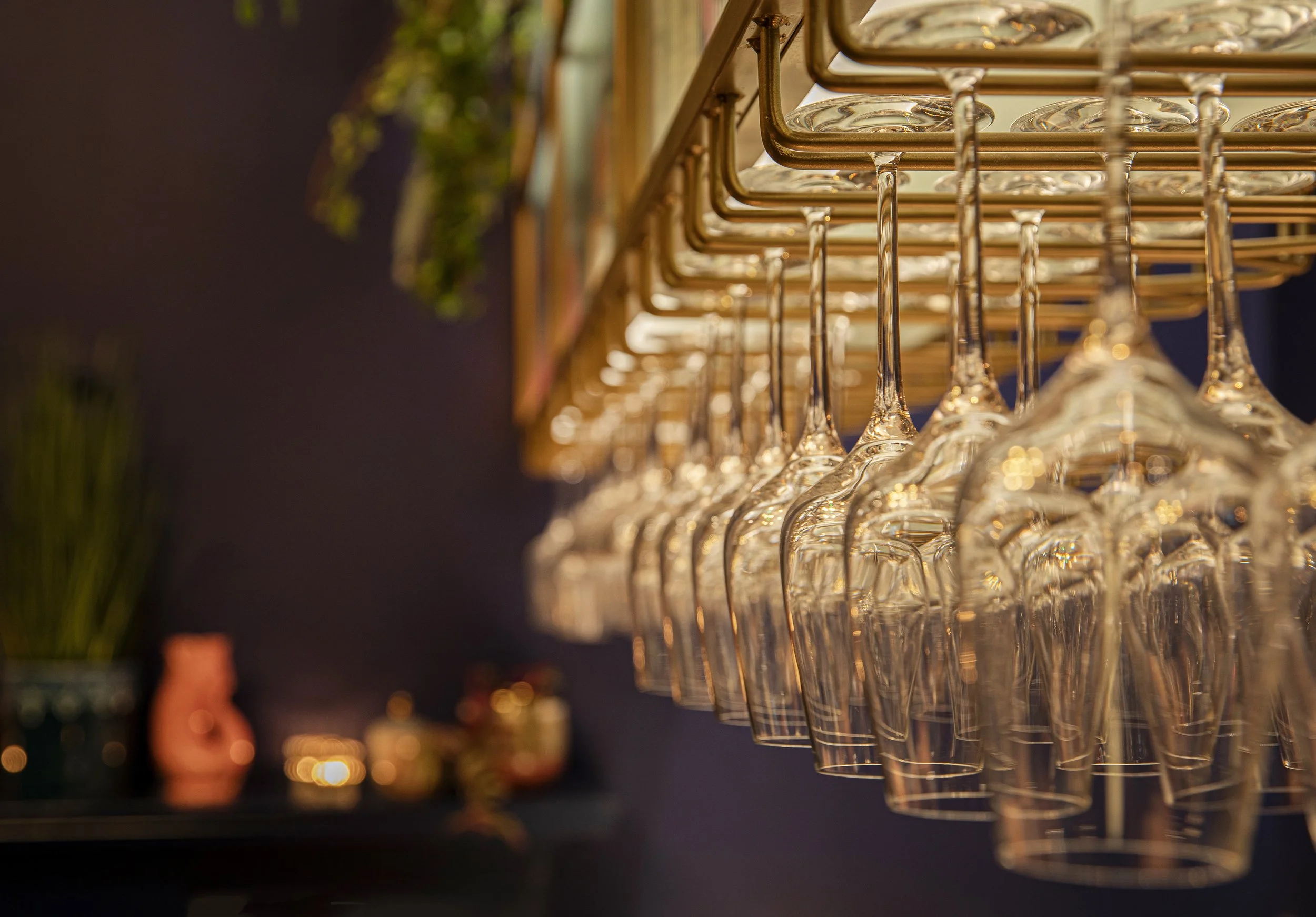 A row of hanging wine glasses on a rack in a bar or restaurant setting with blurred background.