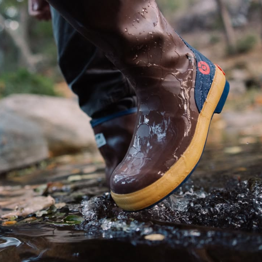 Close-up of a hiking boot stepping into a shallow stream, water splashing around the sole.