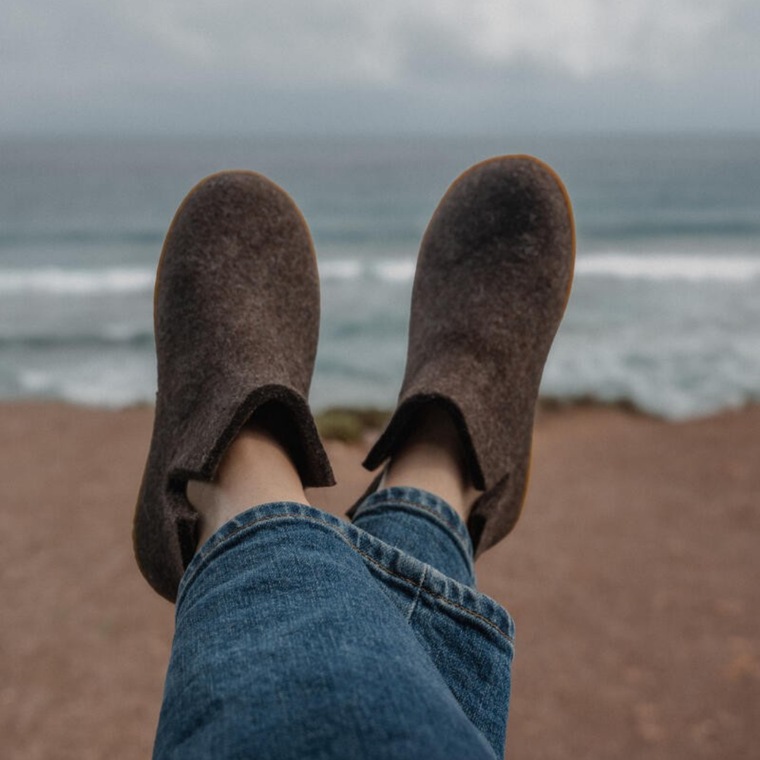 Person relaxing on a ledge overlooking the ocean with their legs and brown slippers visible in the foreground