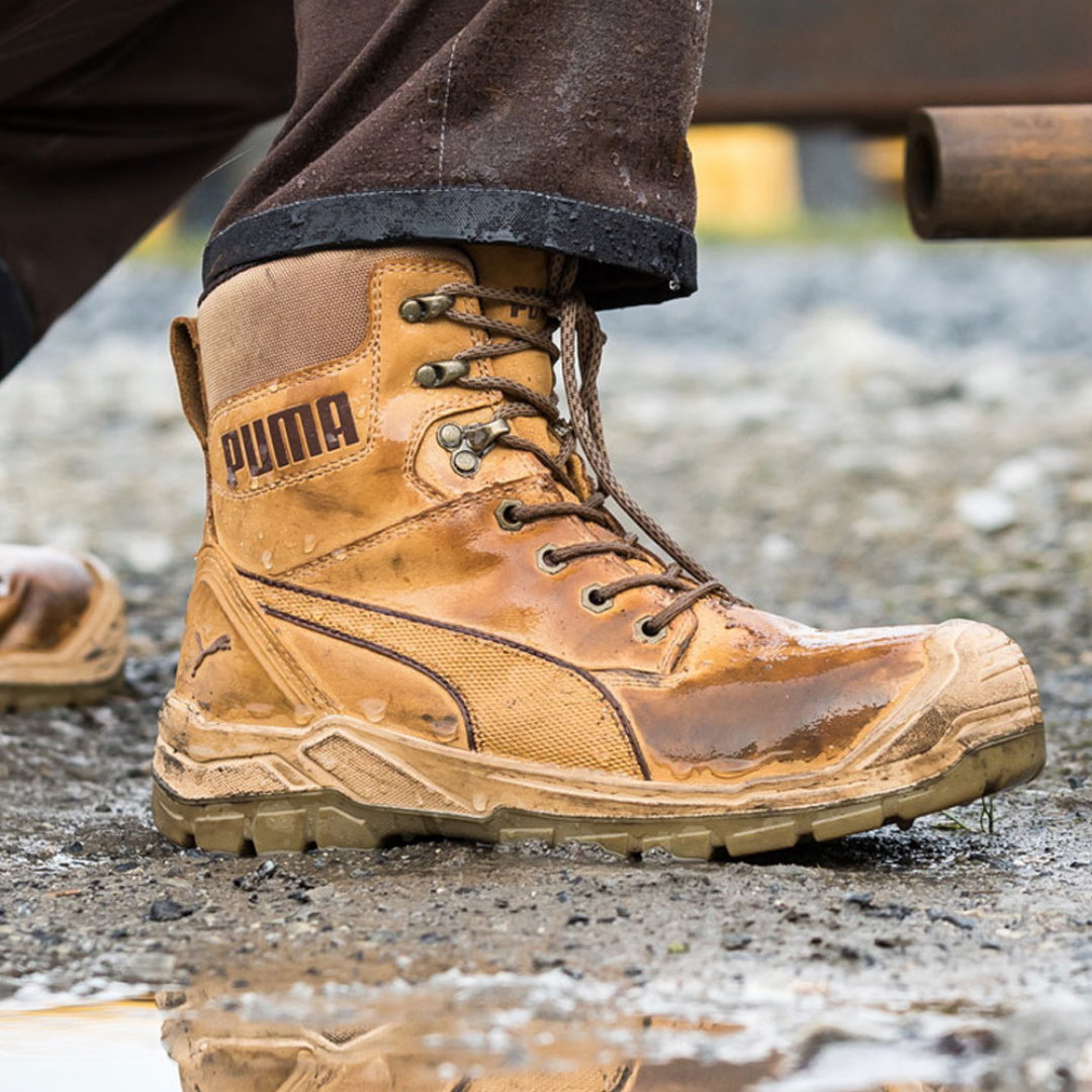 A close-up of a brown PUMA hiking boot on a muddy, gravelly ground.