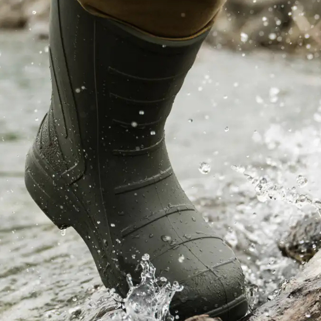 Close-up of a black rubber boot stepping into water, splashing water around.