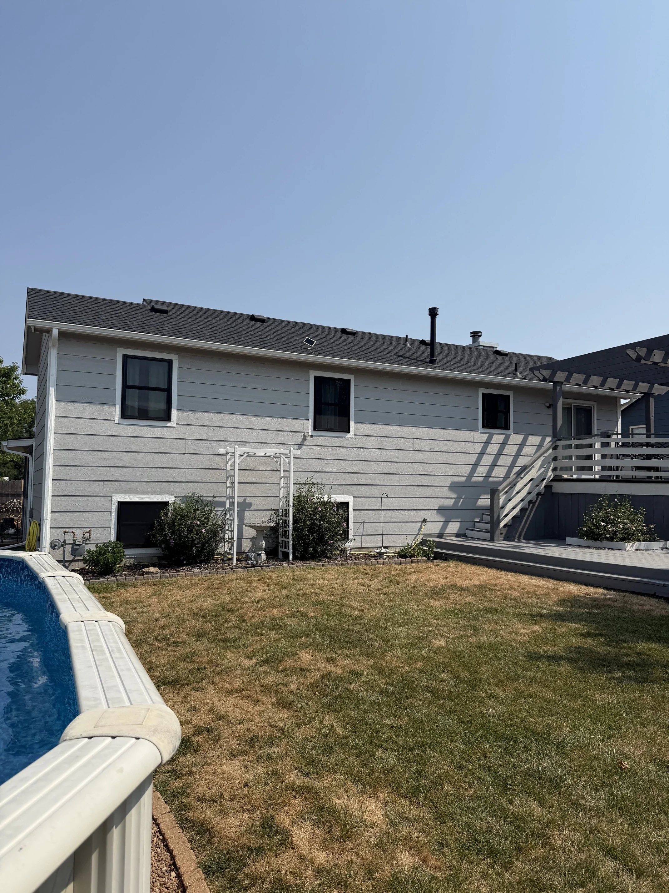 Backyard with a house, solar panels, a deck with stairs, a partially visible swimming pool, and a lawn.