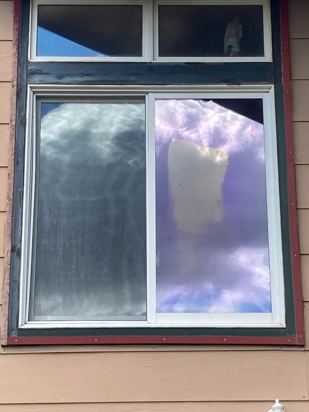 A house window with two panes reflecting the sky and clouds.