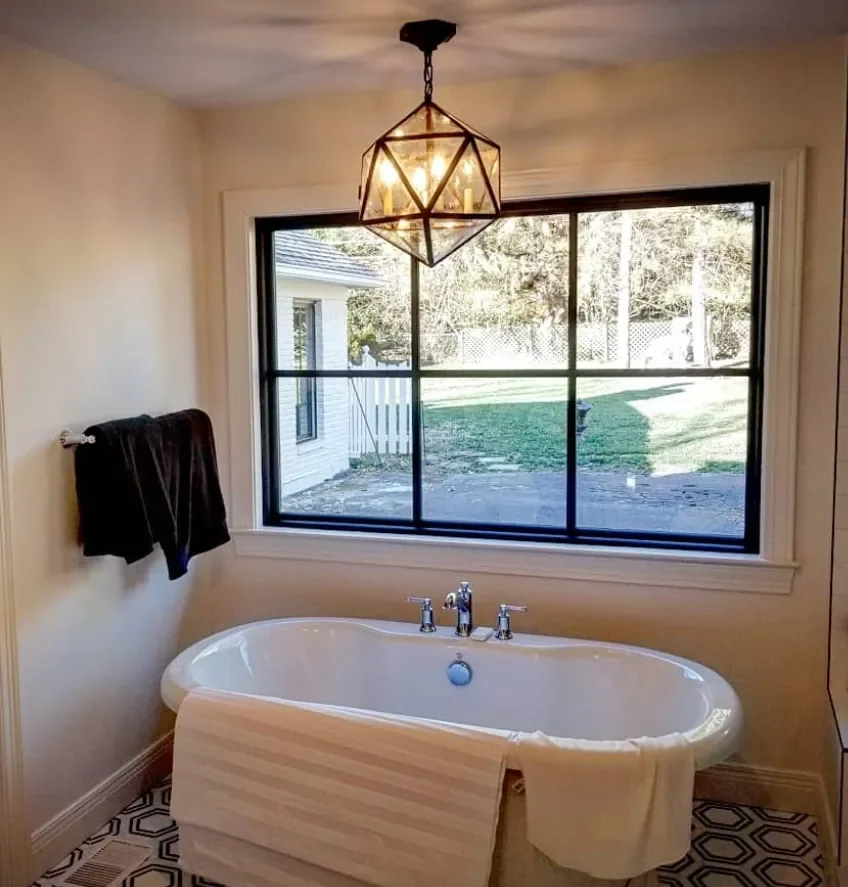 Bathroom with a large window, a white bathtub, a black towel hanging on the wall, and a geometric pendant light fixture.