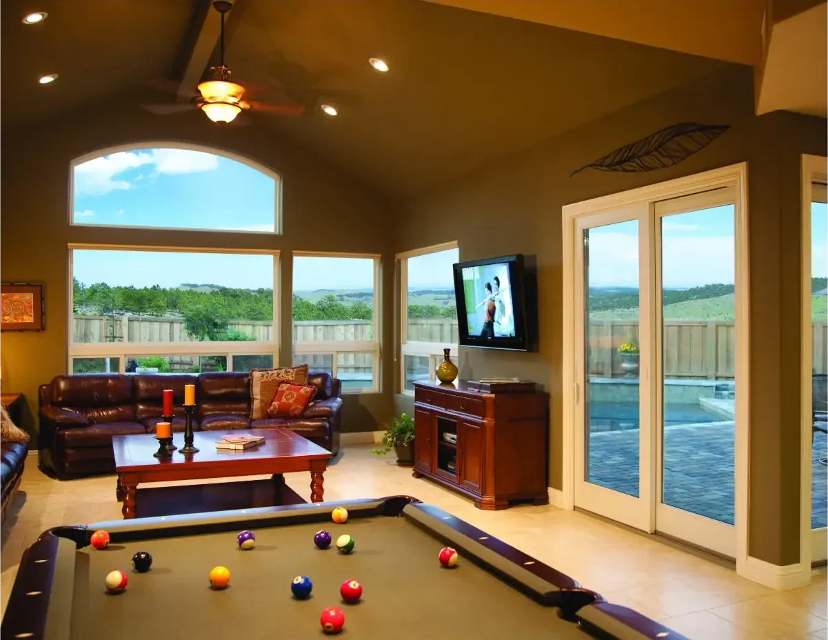 A pool table with balls on it surrounded by white windows and a white patio door