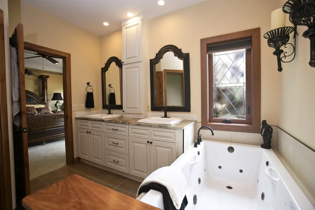 Bathroom with dual sinks, black-framed mirrors, a window, a jacuzzi tub, and decorative wall sconces.