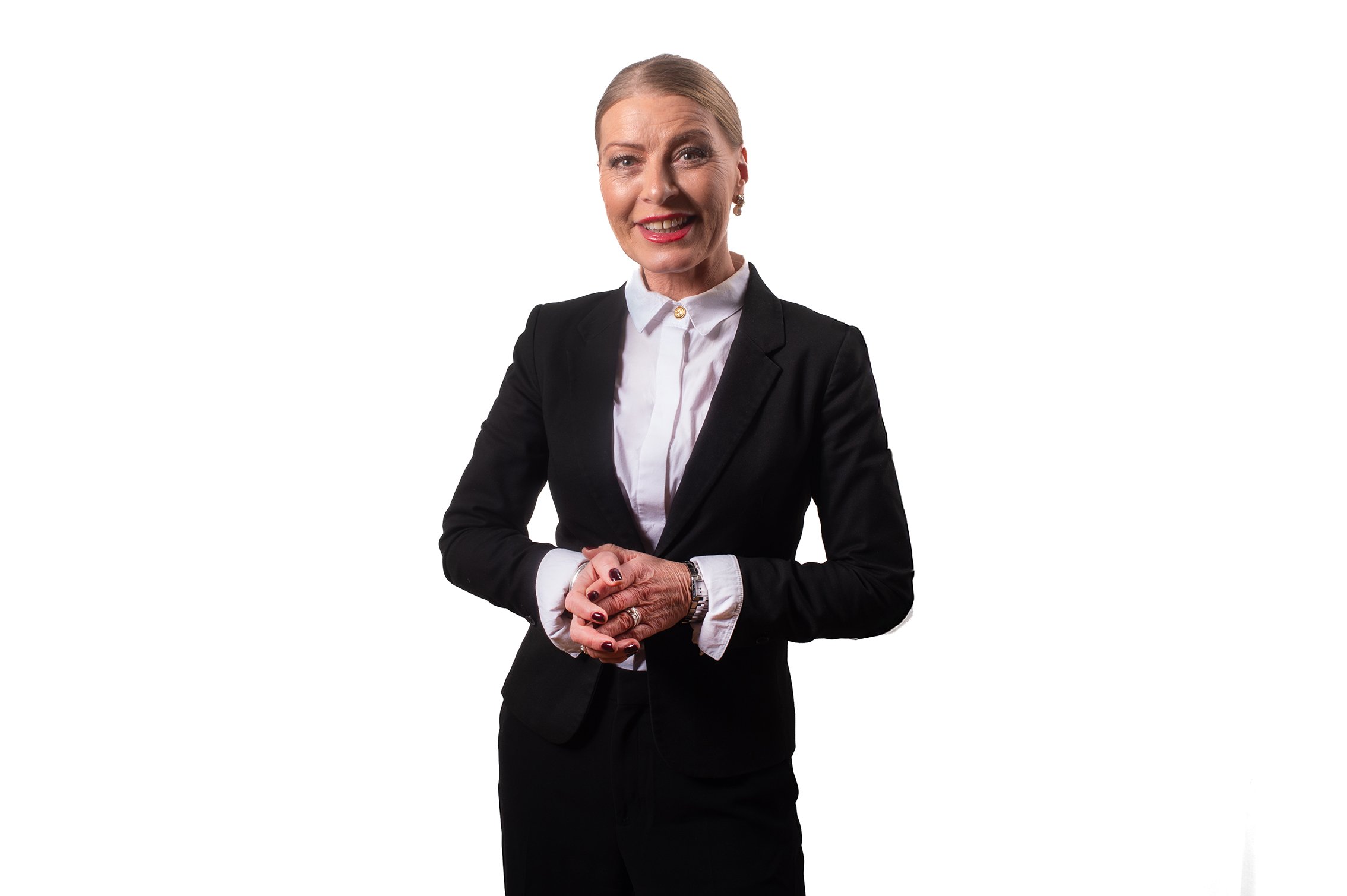En kvinna klädd i svart blazer och vit skjorta, ler och står mot en vit bakgrund.