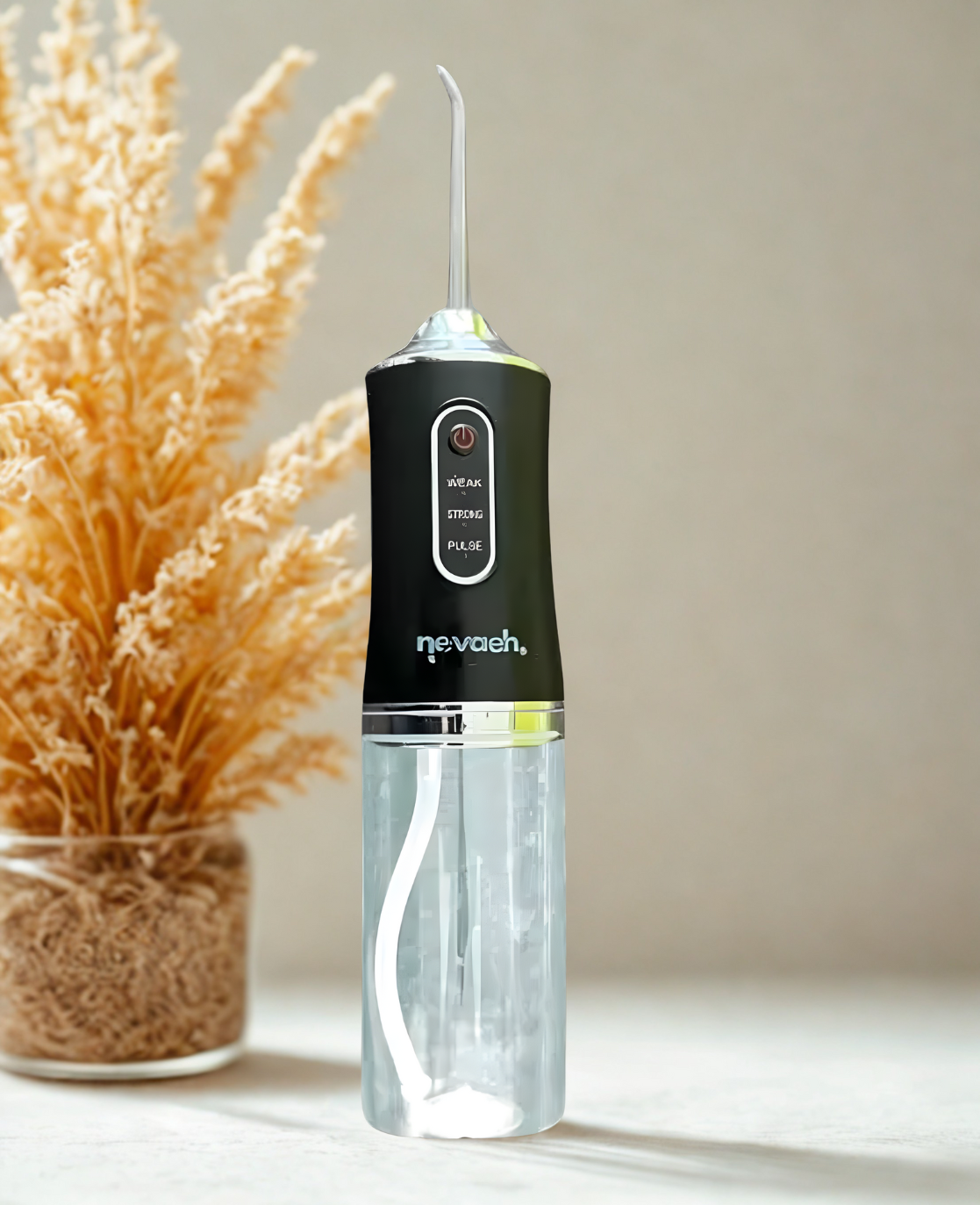 A black and transparent oral irrigator with a digital display and a long nozzle, placed on a white surface next to a pot of dried wheat or grass.