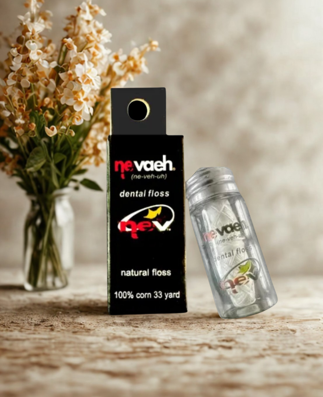 A bottle and container of Nevae dental floss with a vase of dried flowers in the background on a wooden surface.