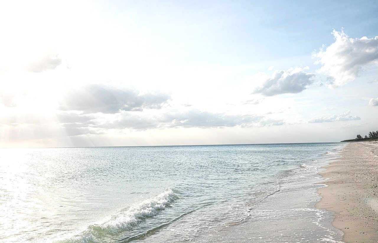 A serene beach scene with light waves crashing on the sandy shore under a partly cloudy sky.