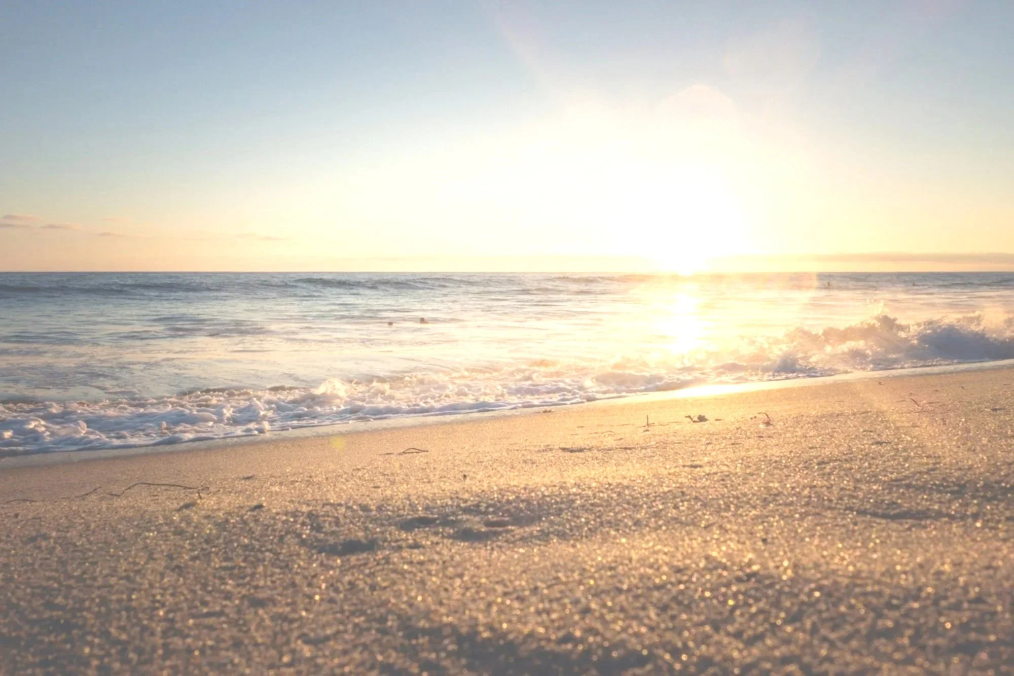 Sunset over the ocean with waves crashing on the sandy beach.