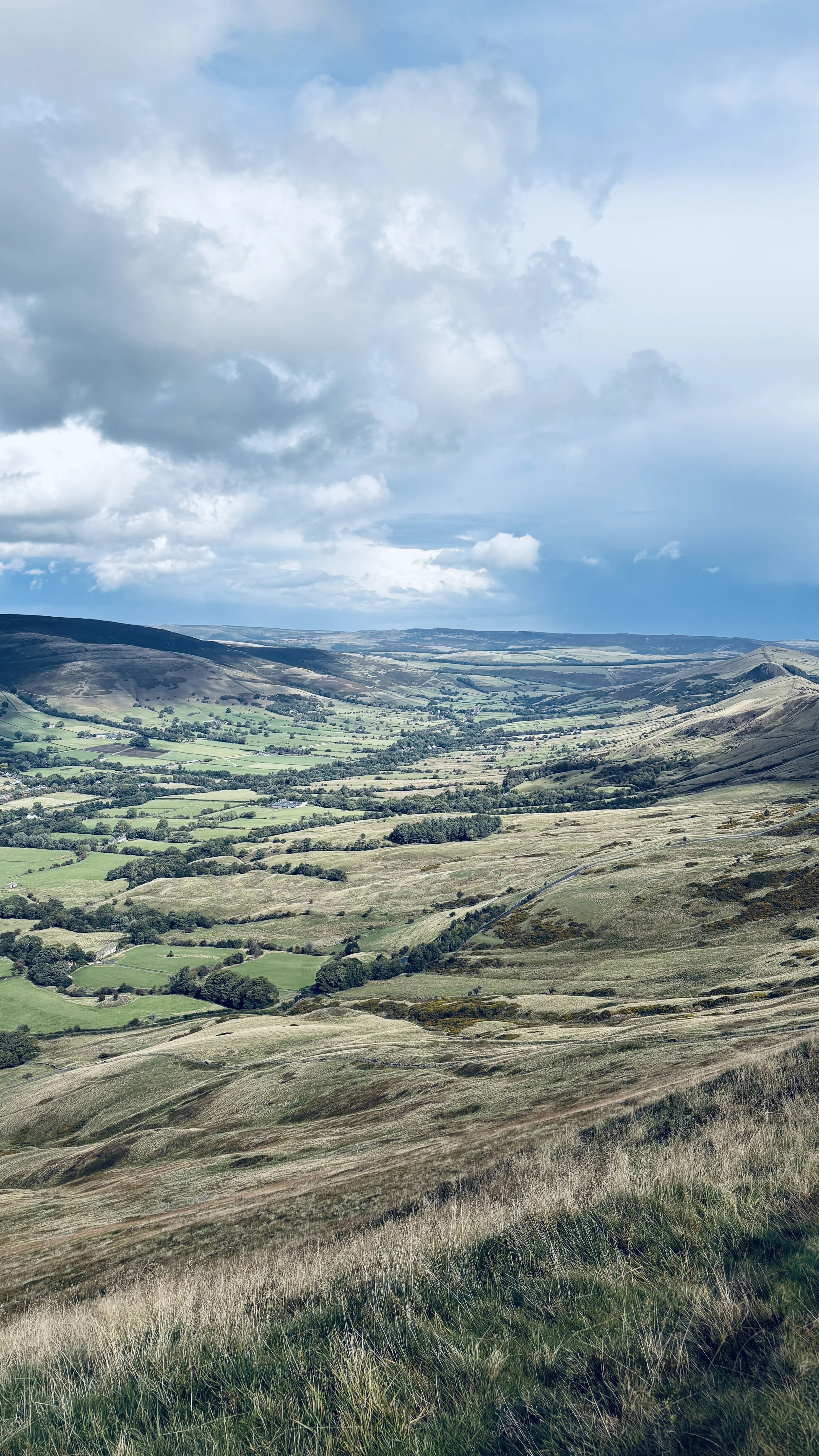 Scenic landscape of rolling green hills and valleys under a cloudy sky.