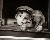 niño triste mirando por la ventana con un elefante de juguete