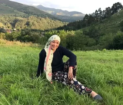 paciente de cancer con un pañuelo en la cabeza sonriendo en un prado verde