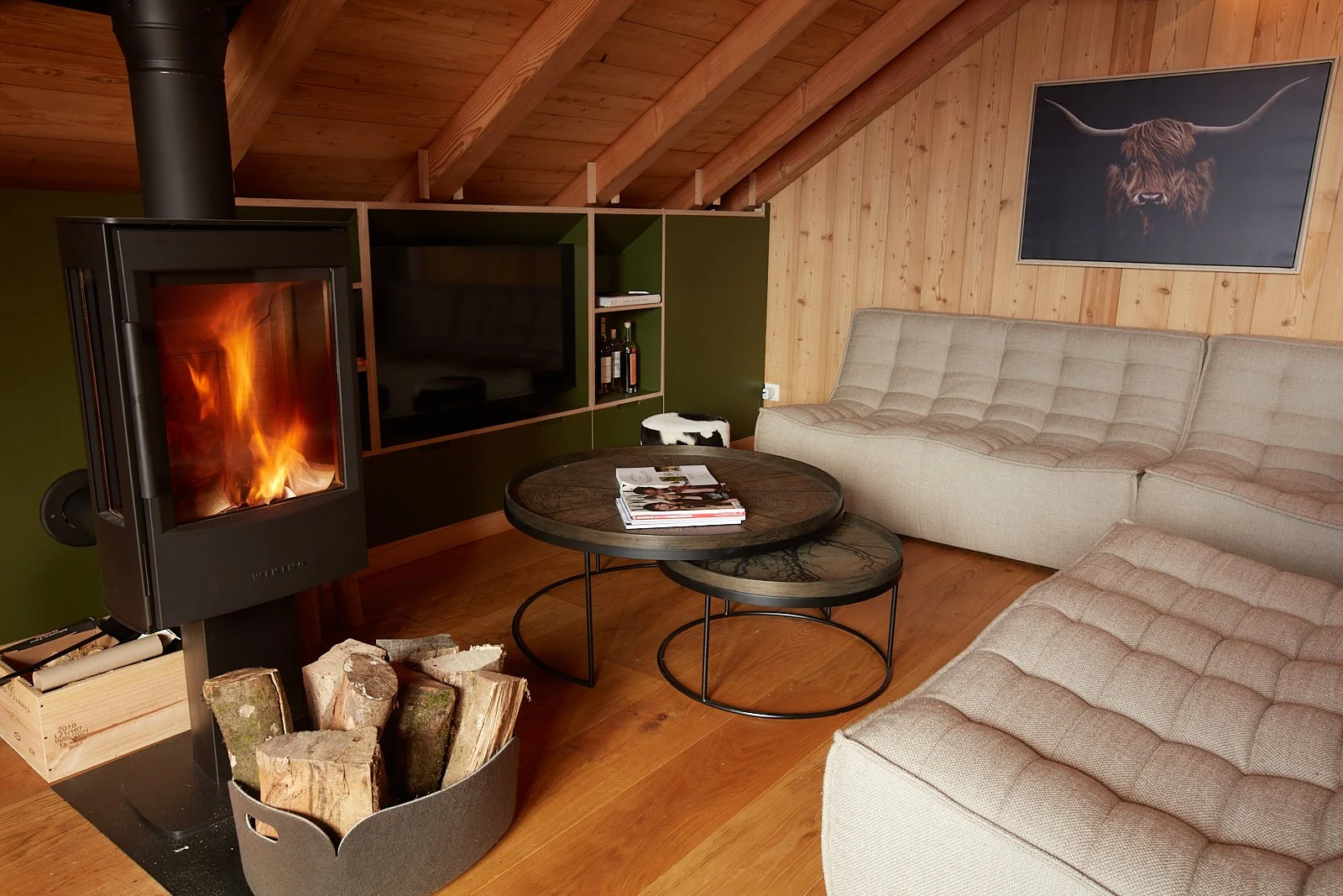 Salon avec cheminée en marche, canapé beige, tables basses en bois, murs en bois, tableau d'un bison avec cornes sur le mur.