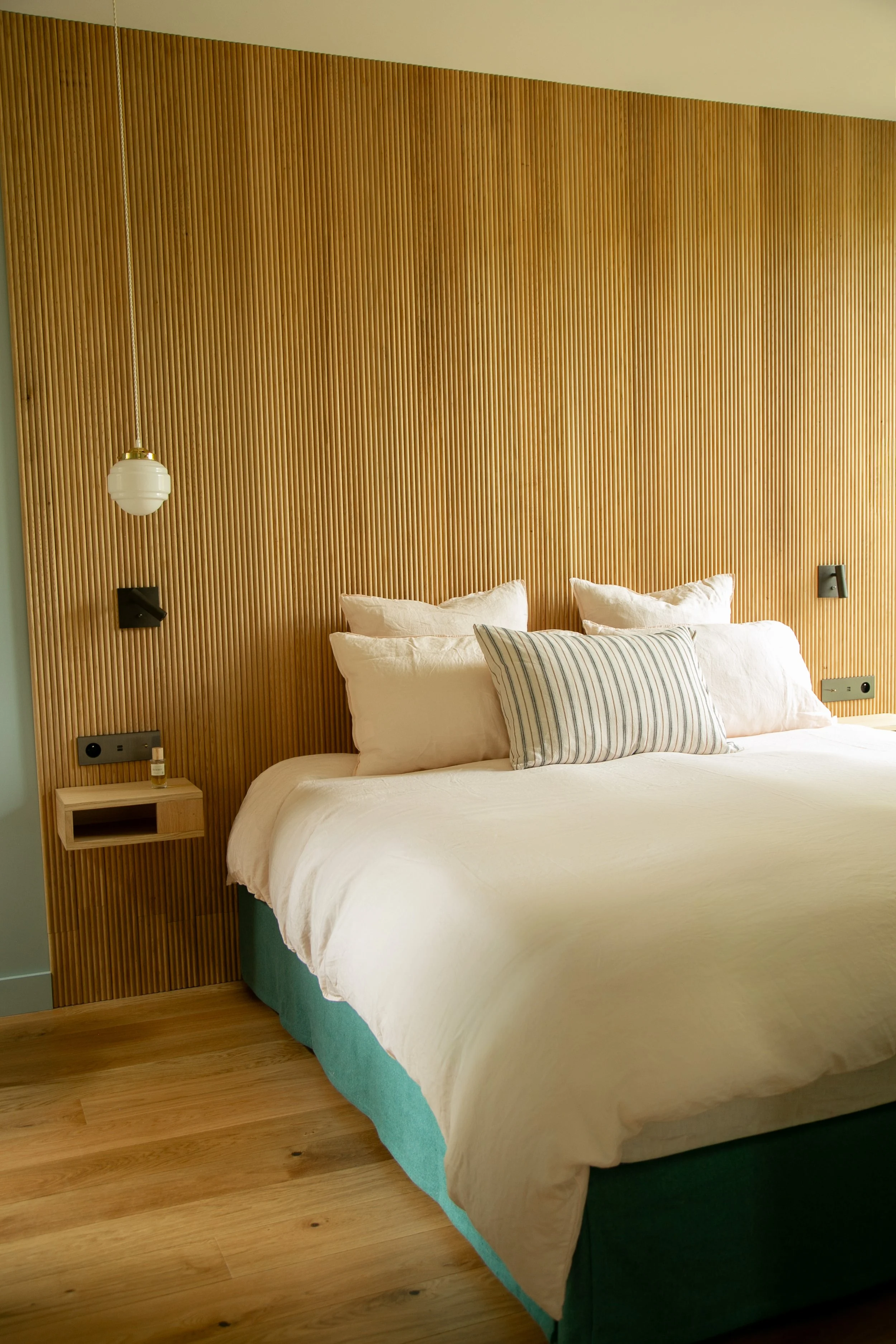 Lits dans une chambre avec tête de lit en bois naturelle, murs en bois sculpté, lampe suspendue et table de nuit en bois.