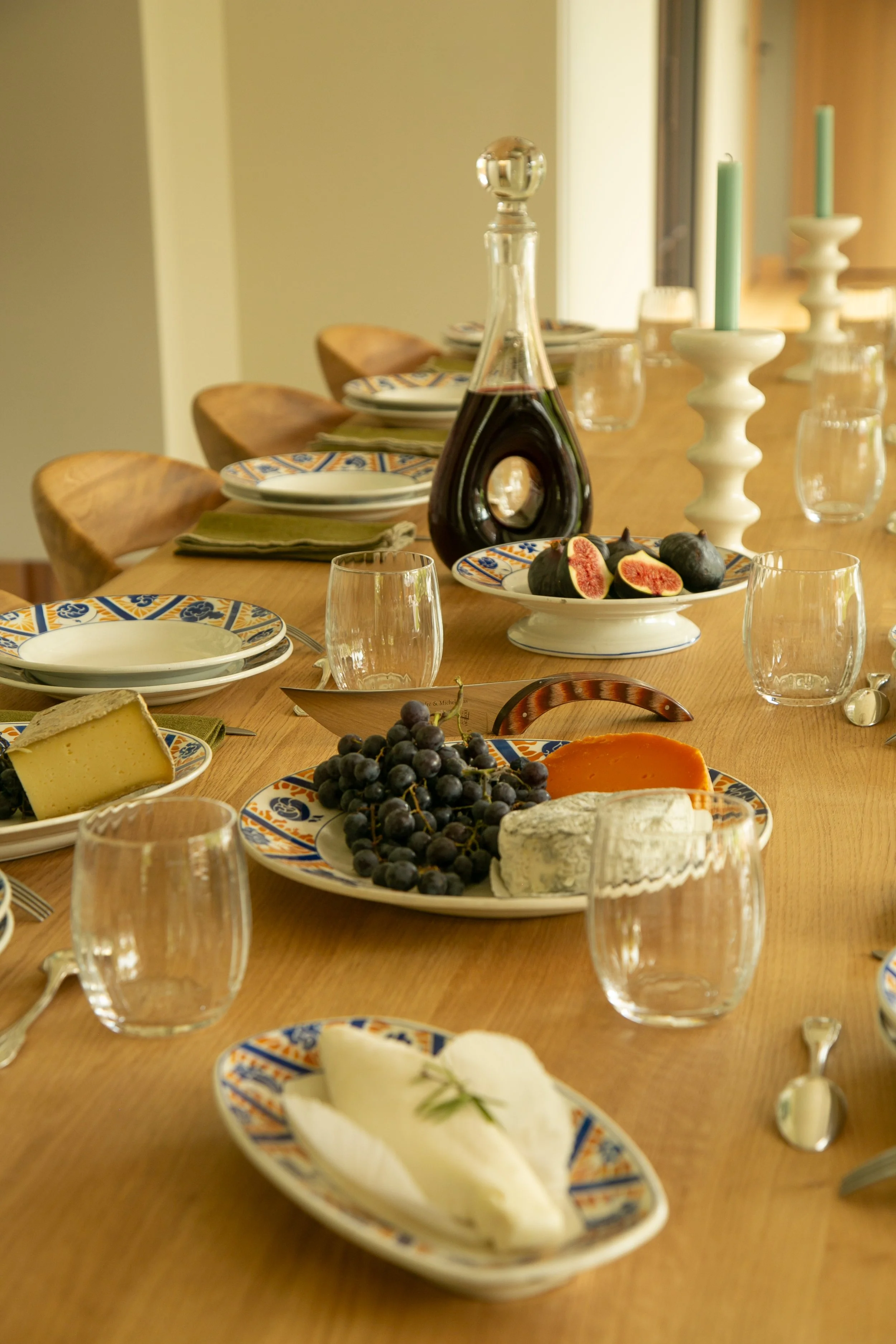 Table de dîner avec des plats de fromages, des raisins, des figs, des bougies et une bouteille de vin.