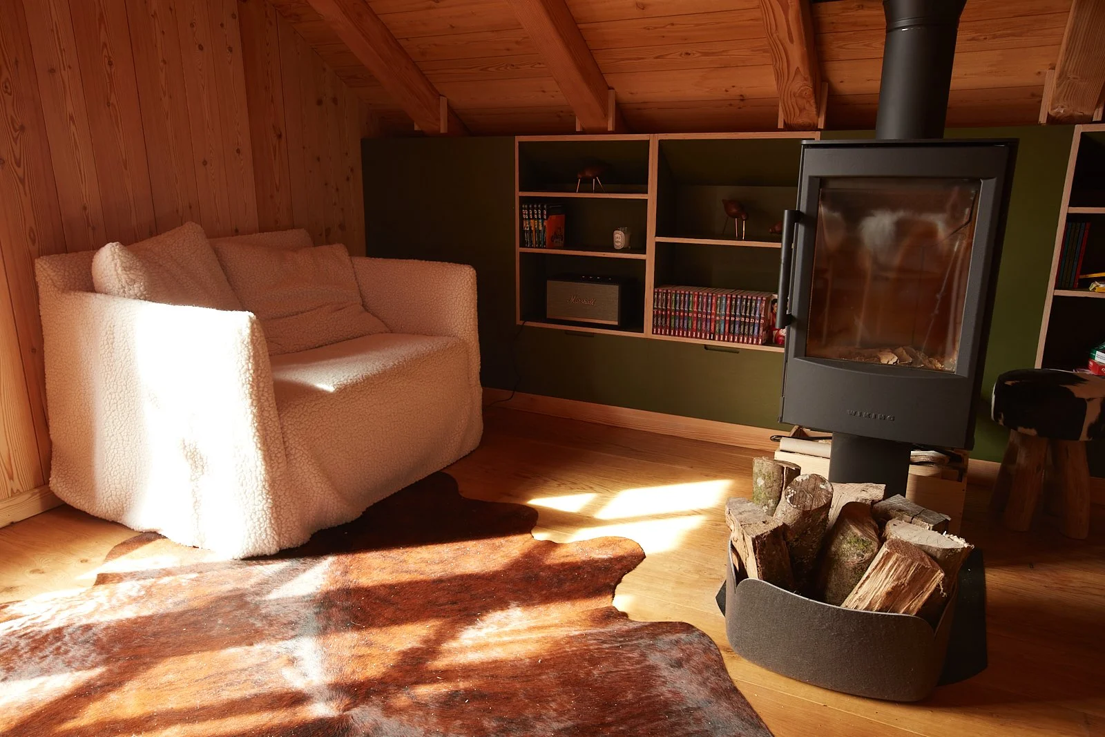 Salon de style cocon dans une cabane en bois avec cheminée à bois et fauteuils confortables