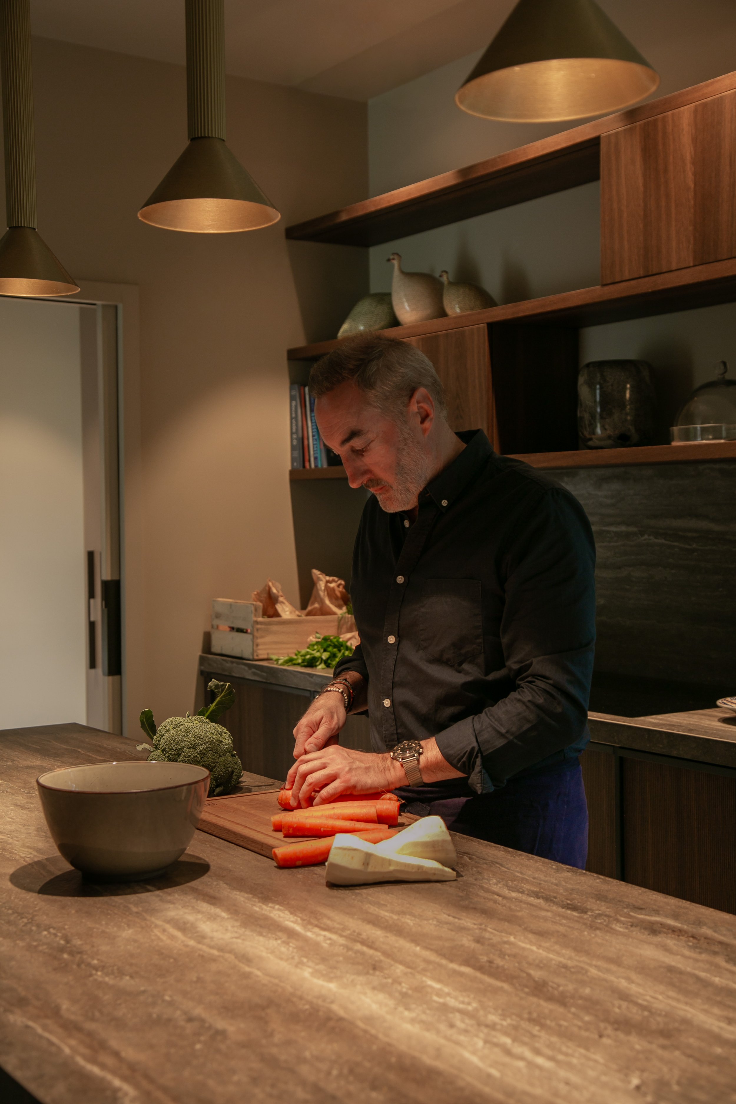 Un homme prépare des légumes sur un plan de travail en cuisine moderne.