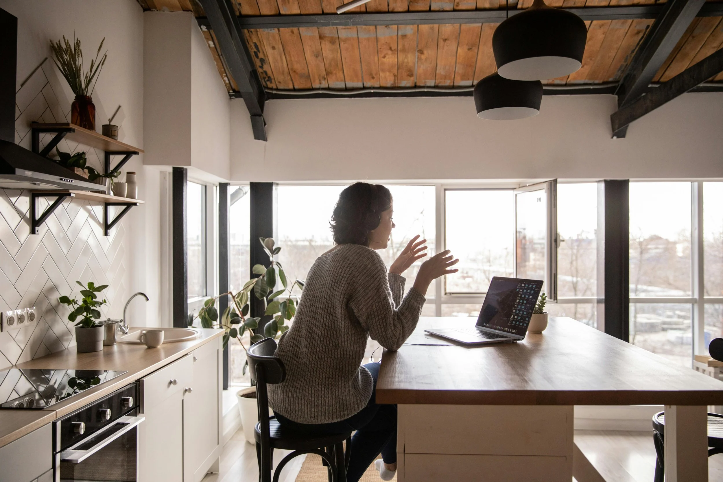 Woman with headphones talking on a video call at a kitchen island with a laptop