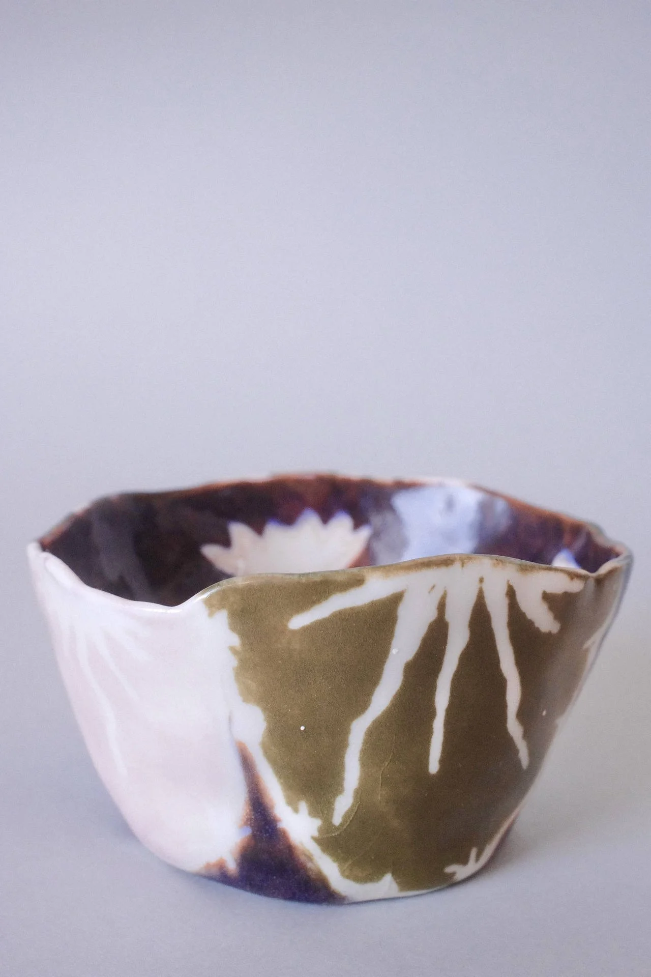 Hand-pinched porcelain cup with a flat base and irregular rim in brown, blue, pink, lavender and white