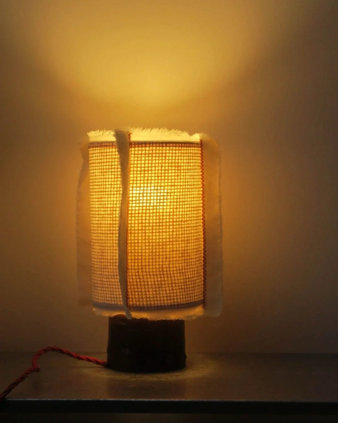 Trama Lamp

Made by Benedetta Ficarelli in London the Trama Lamp combines a keuper red stoneware base with a checkered rattan structure and a hand sewn natural cotton lampshade. The piece balances material contrast and function through a clear and co