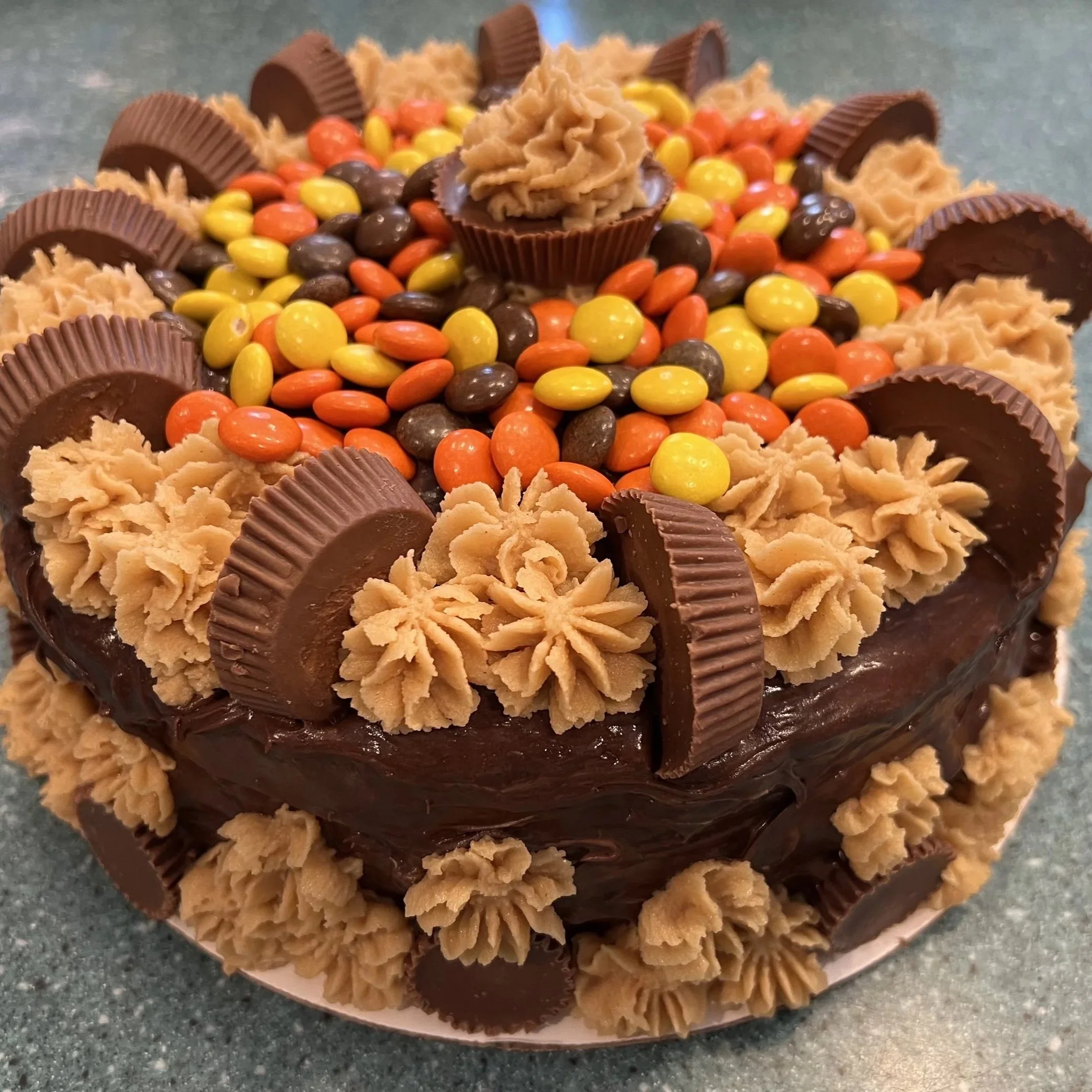 Chocolate cake decorated with Reese's peanut butter cups, peanut butter frosting, and candy-coated chocolates in orange, yellow, and brown.
