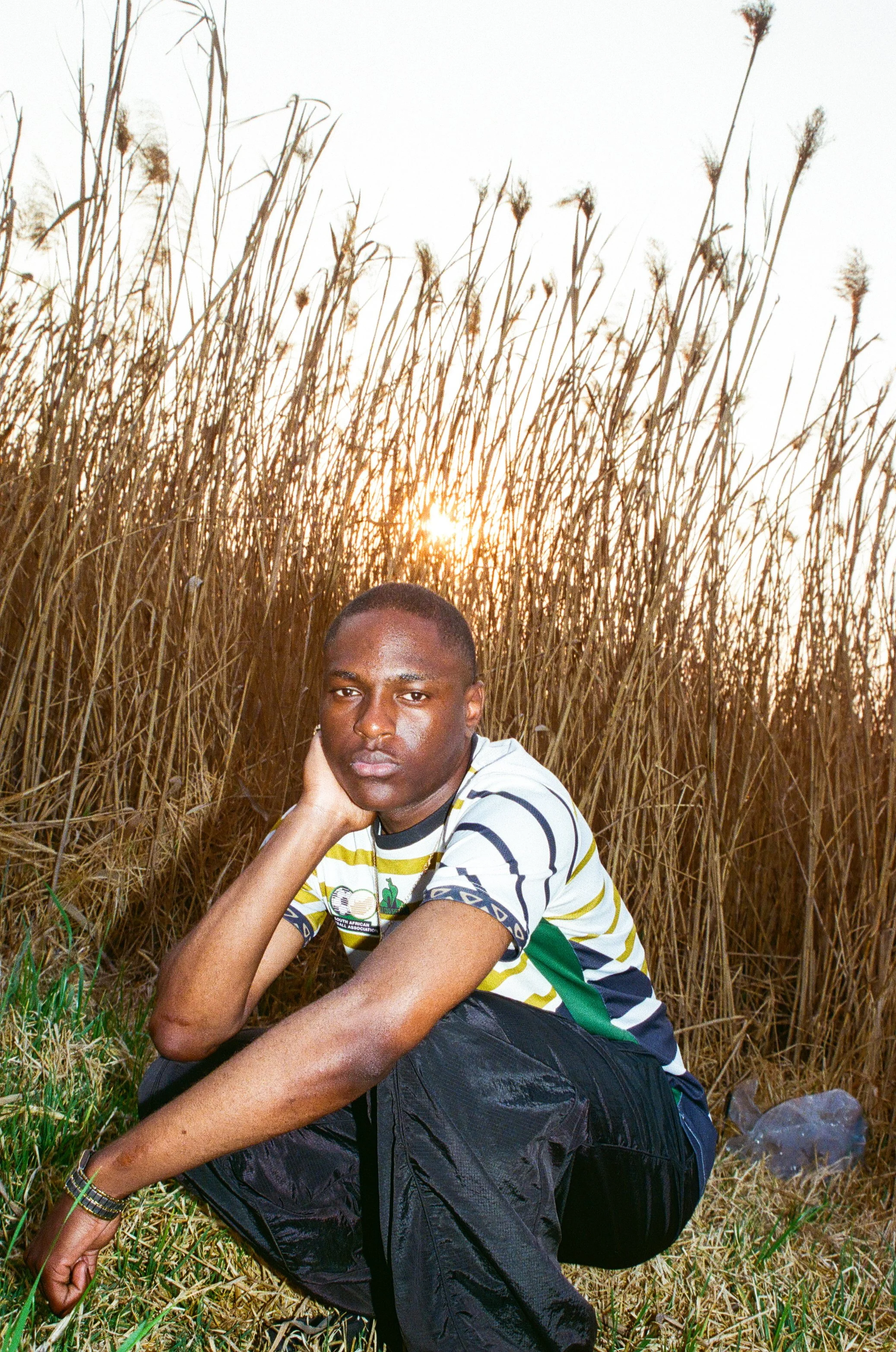 Joshua Futura crouches in a field of tall grass or reeds with the setting sun in the background.