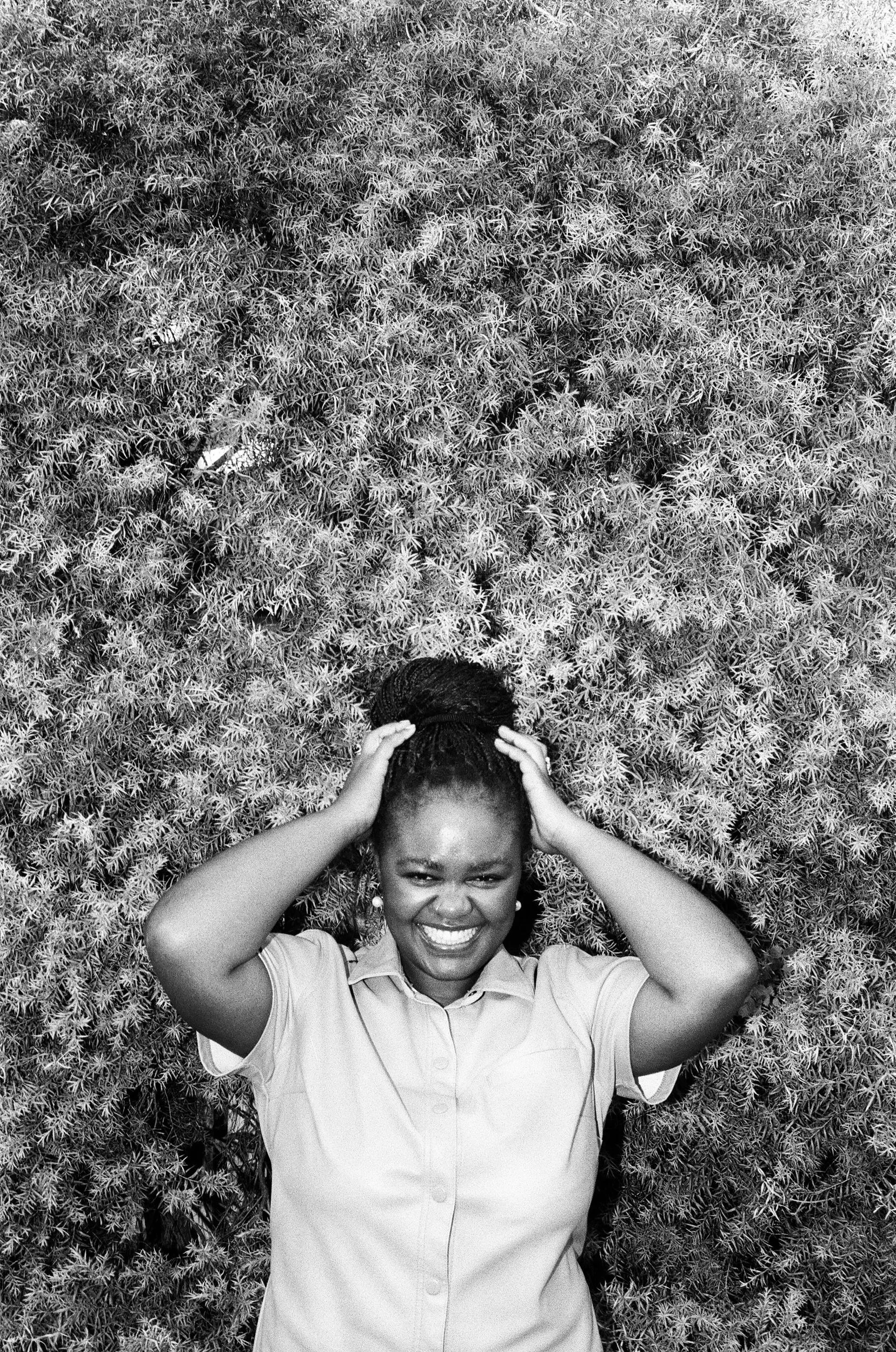 Zizipho Bam holding her head, standing in front of dense, spiky foliage.