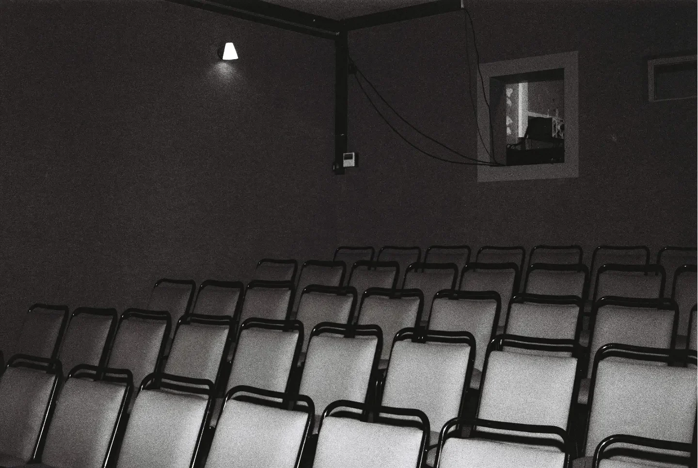 Empty chairs in a dark room with a screen and a window on the wall.