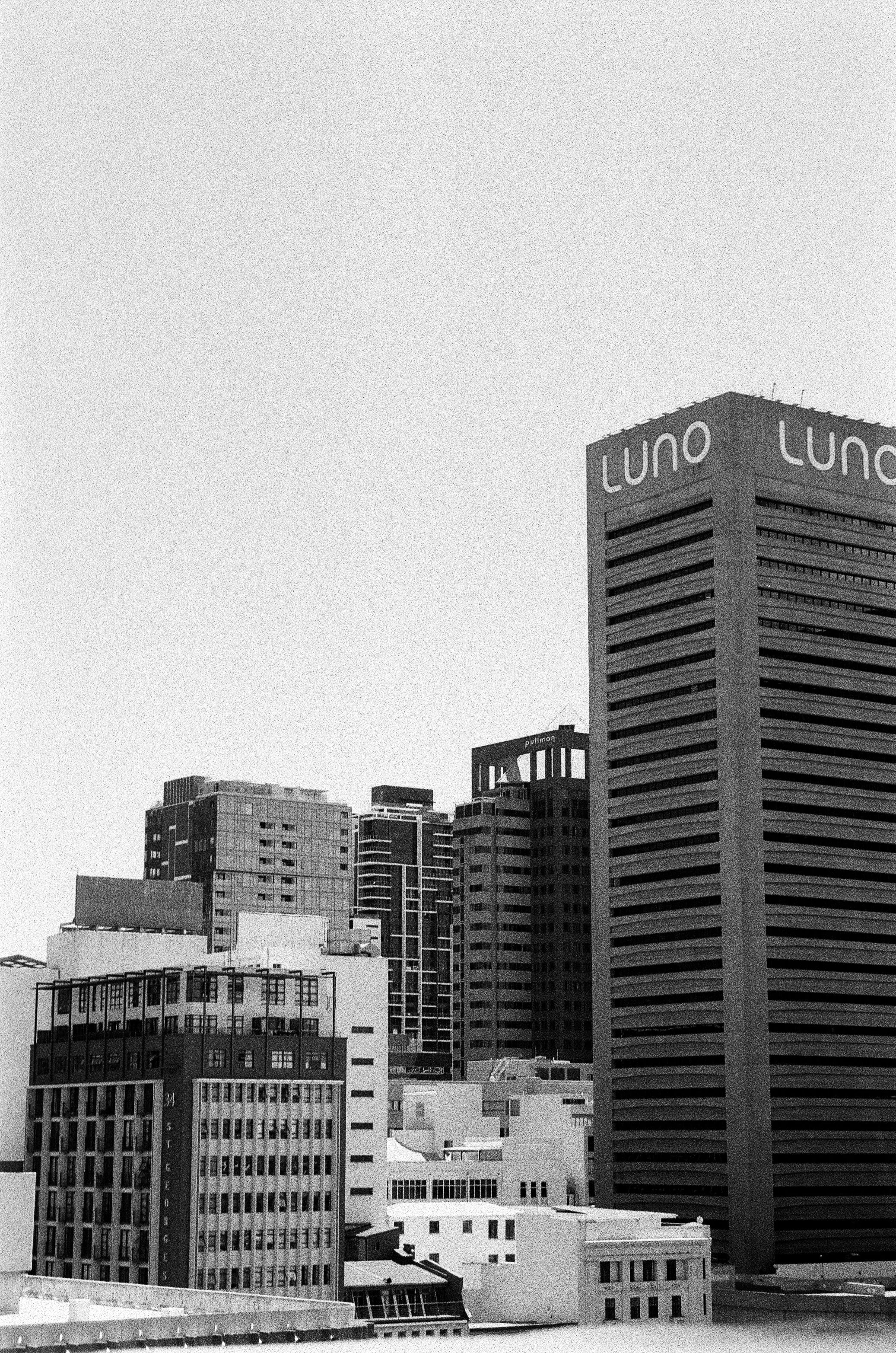 Black and white photo of a city skyline with various high-rise buildings, including a building with the sign 'LUNO' at the top.