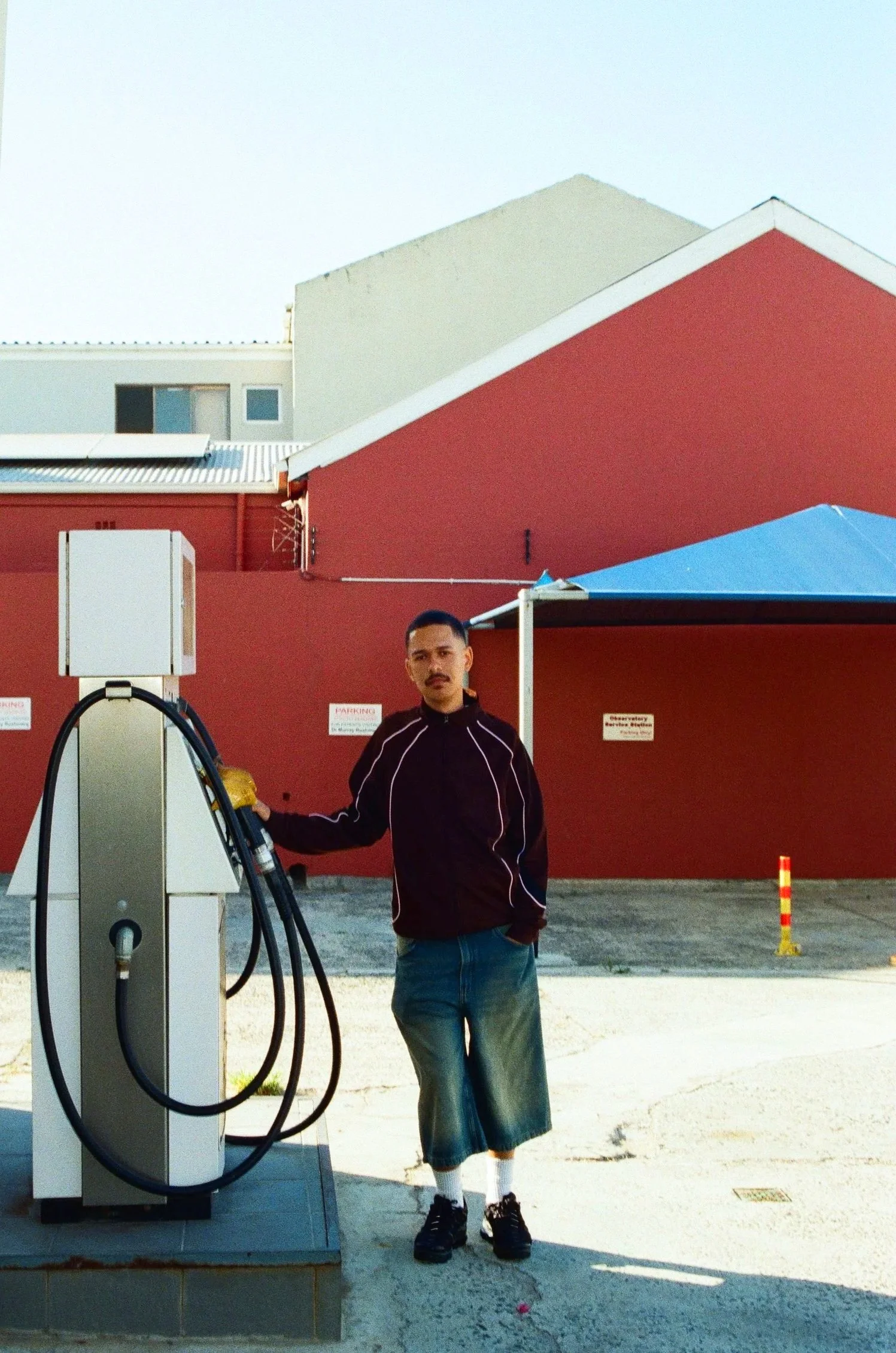 Jarry Pitboi standing next to an electric vehicle charging station outside a red building with a blue canopy.