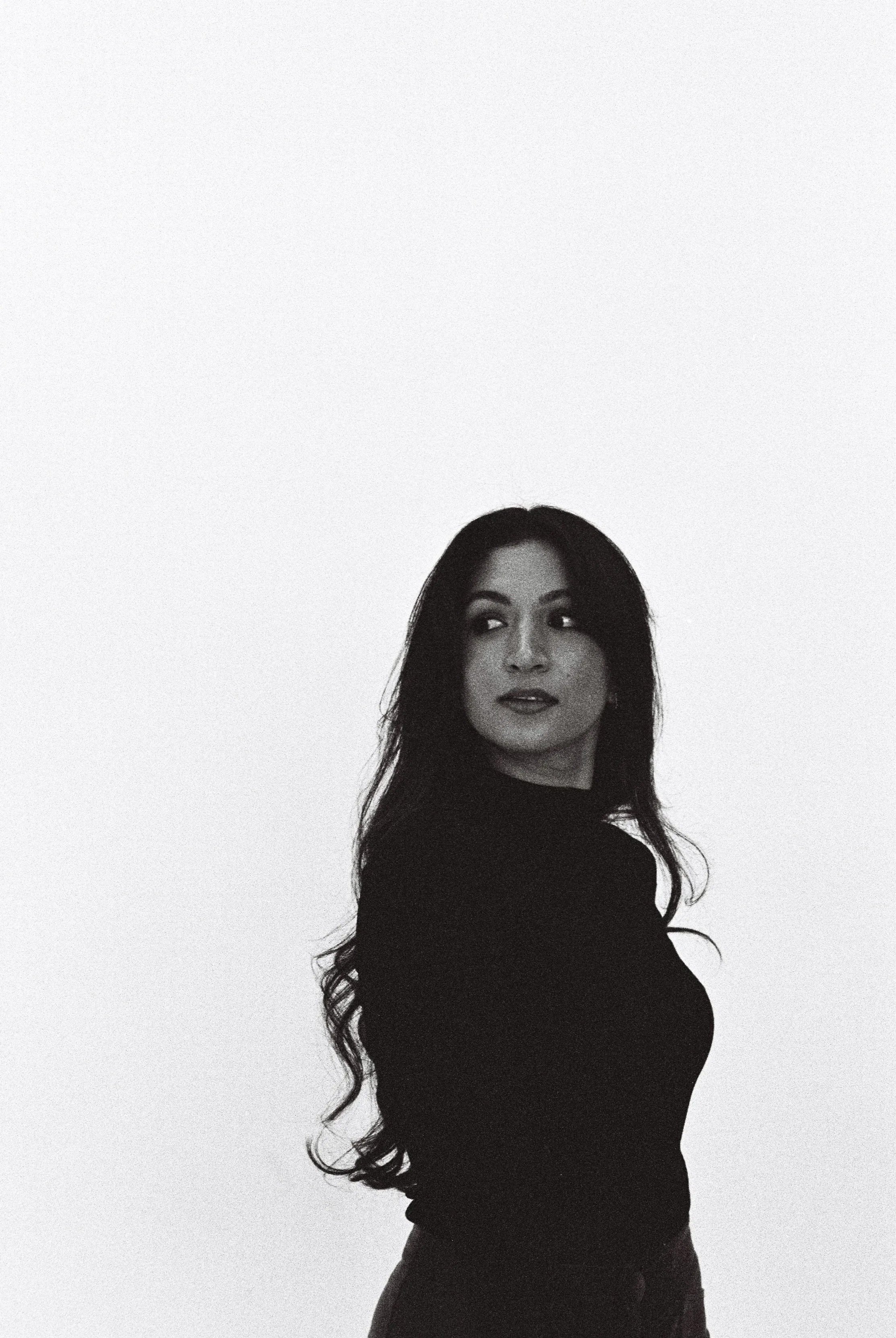 Black and white photo of a woman with long wavy hair looking over her shoulder.