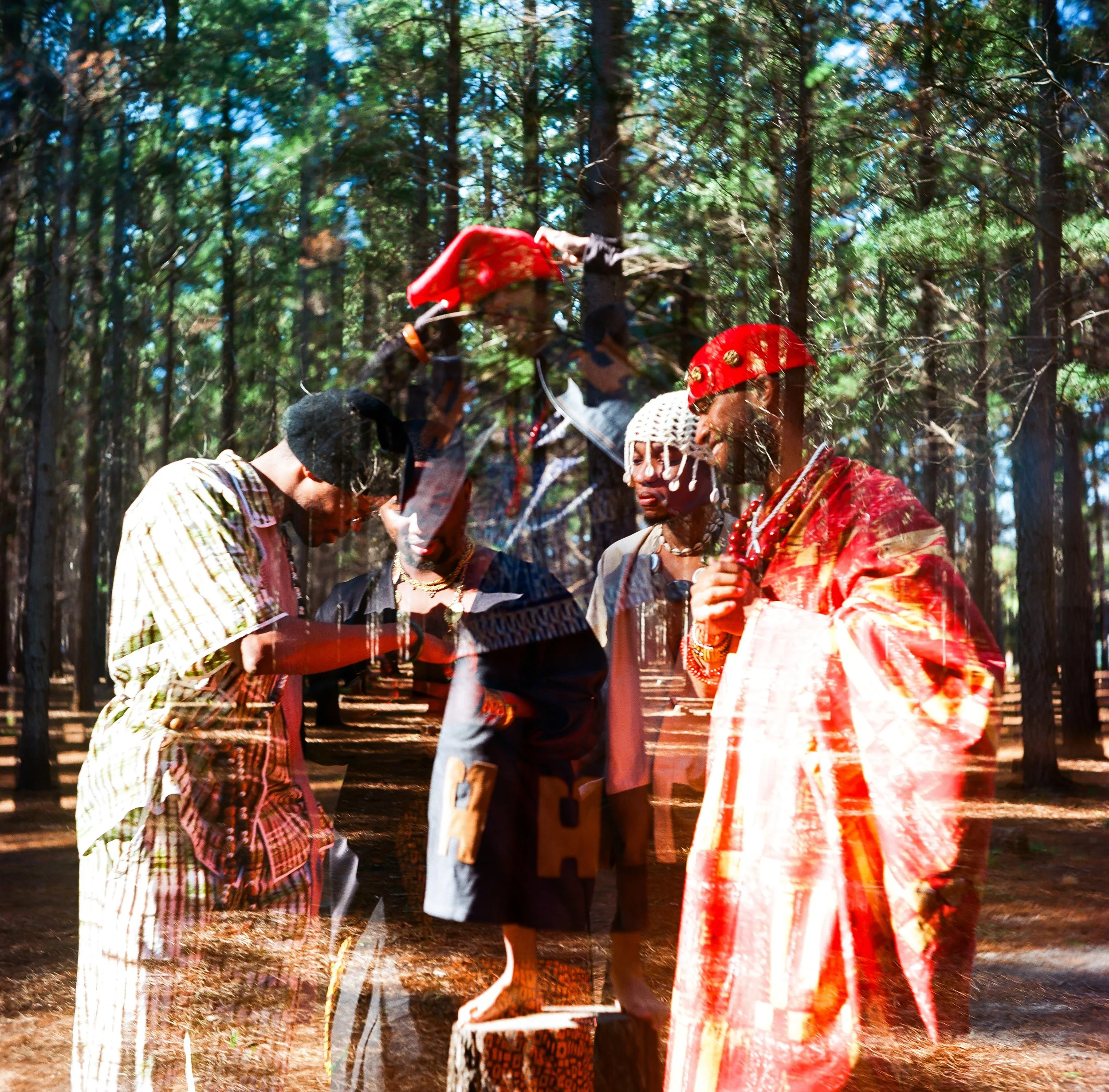 Kujenga in traditional African clothing, standing in a forest, engaged in a cultural ritual or discussion, with vibrant attire and headpieces.