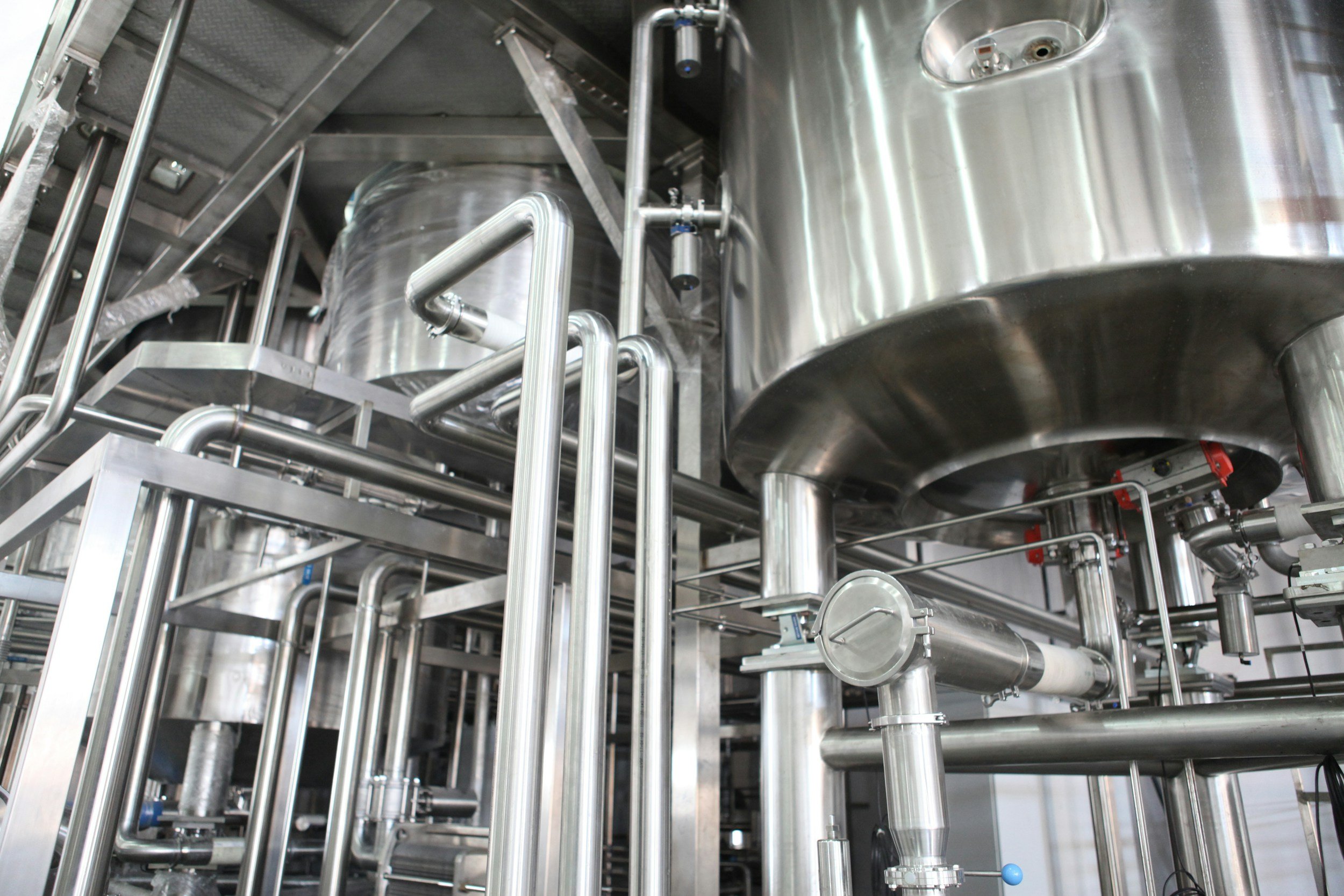 Industrial stainless steel tanks and interconnected piping system in a manufacturing or processing facility.