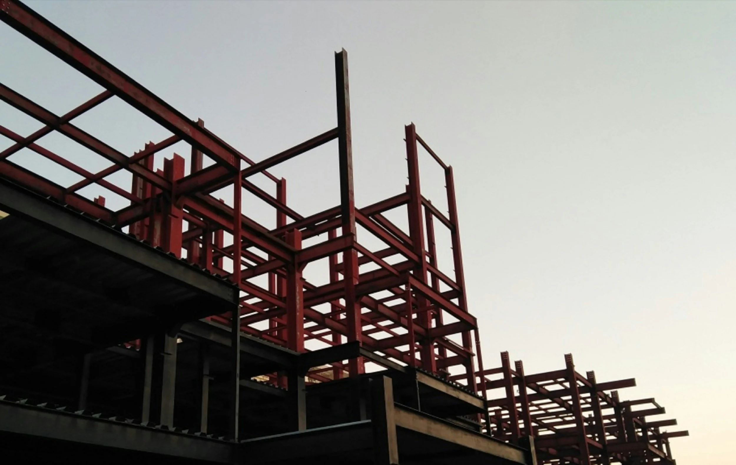Construction site with red metal framework and scaffolding against a pale sky.