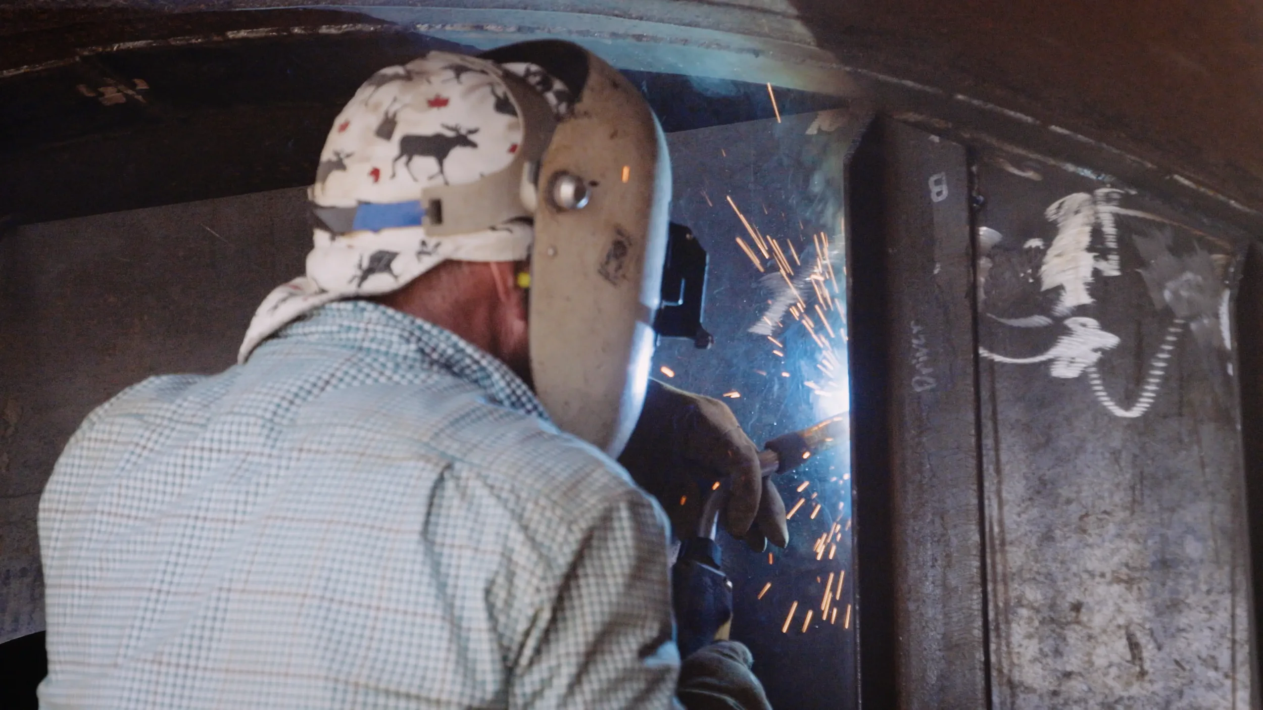 A welder welding metal while wearing a protective helmet and gloves, with sparks flying from the welding process.