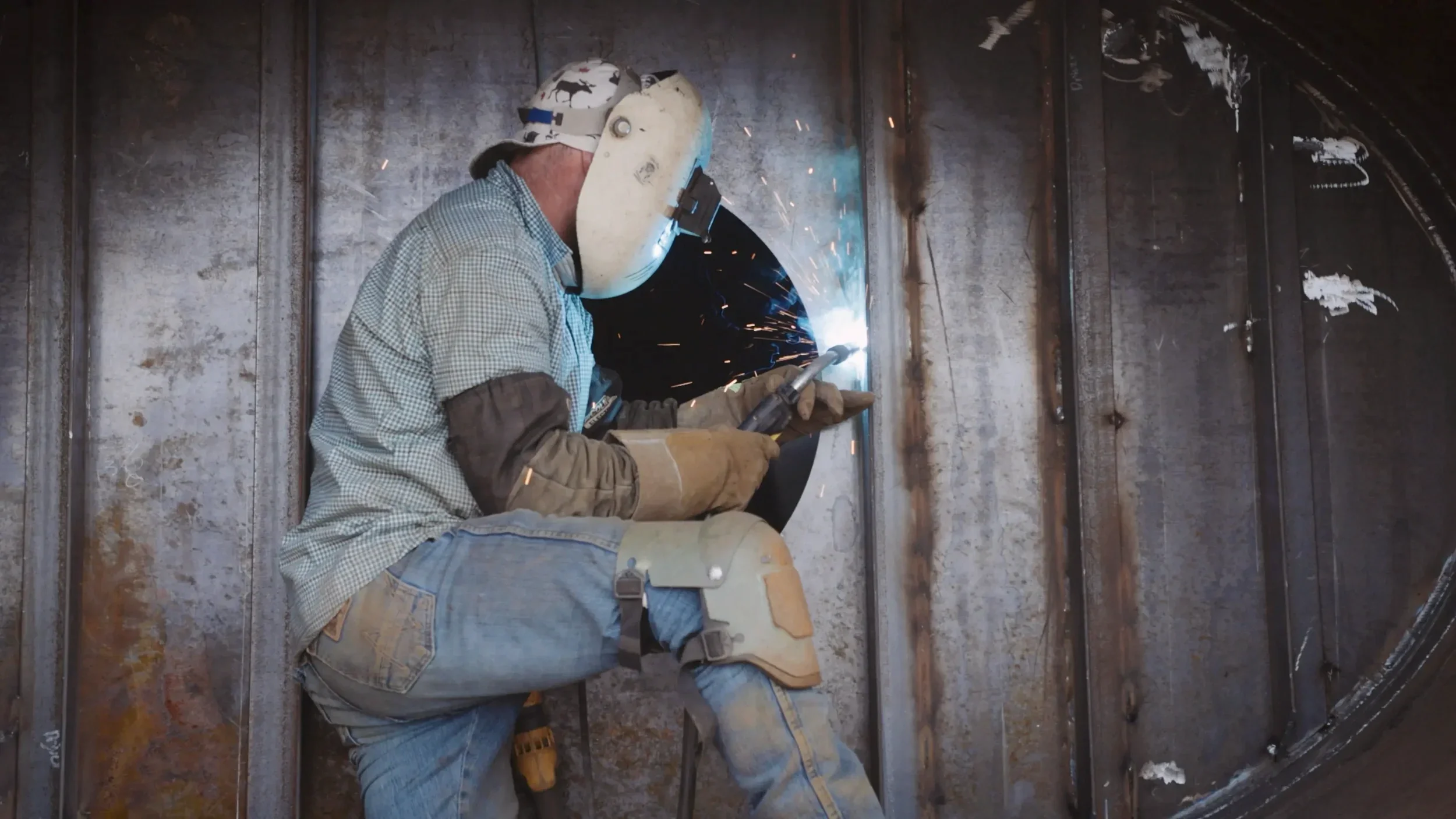 A worker in protective gear welding a metal baffle or weir inside a liquid transport tank.