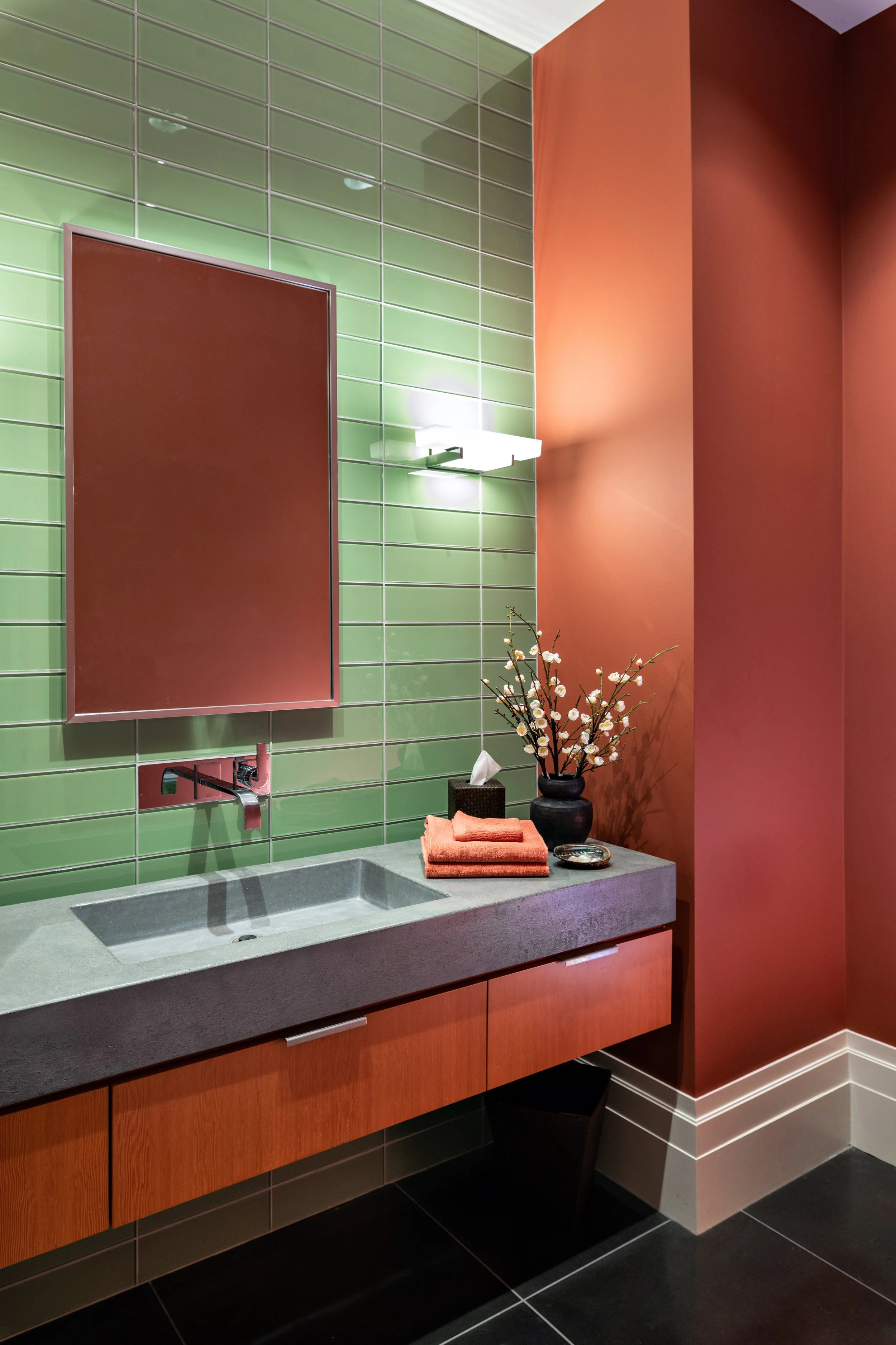 Lincoln Modern Powder room with green glass stacked tile, rust-colored walls and near black large format tile on the floor. Room features a floating wood vanity with a concrete countertop and integrated
sink creates, Contemporary wall-mounted lightin