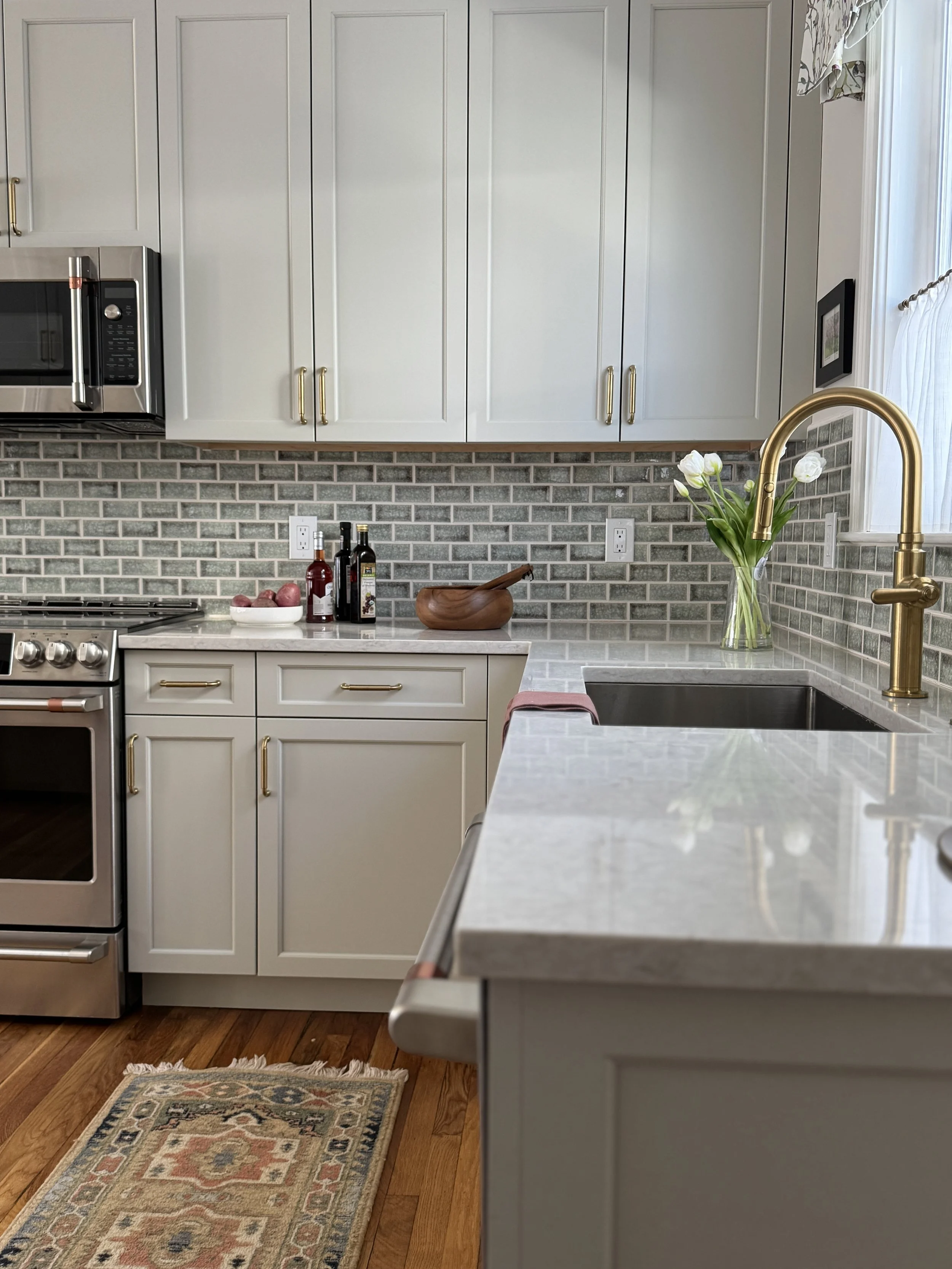 Open kitchen and dining room with pale green cabinetry, brass faucet, and increased natural light after wall removal