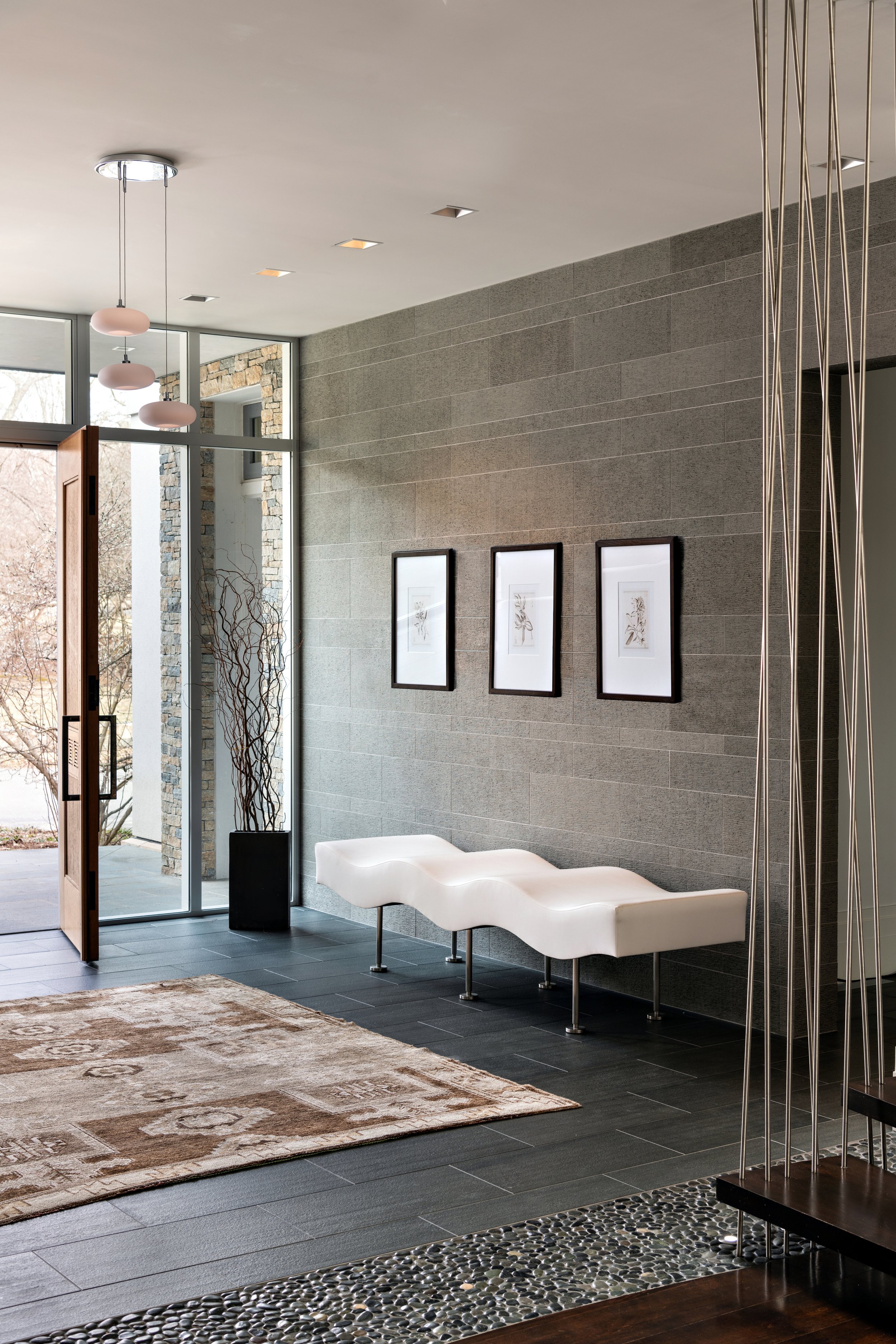 Lincoln entry with limestone accent wall, upholstered wave-shaped bench, tile-and-stone floors, and chrome lighting.