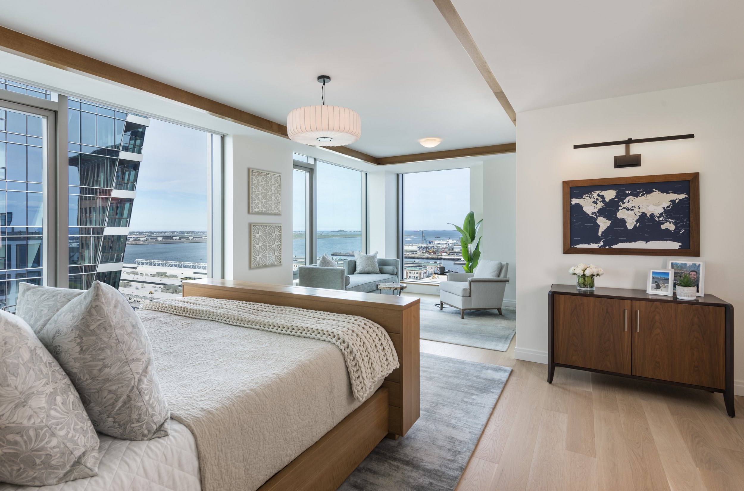 Seaport primary bedroom with custom rift-oak floating bed, seafoam sitting area, silk rug, and harbor views.