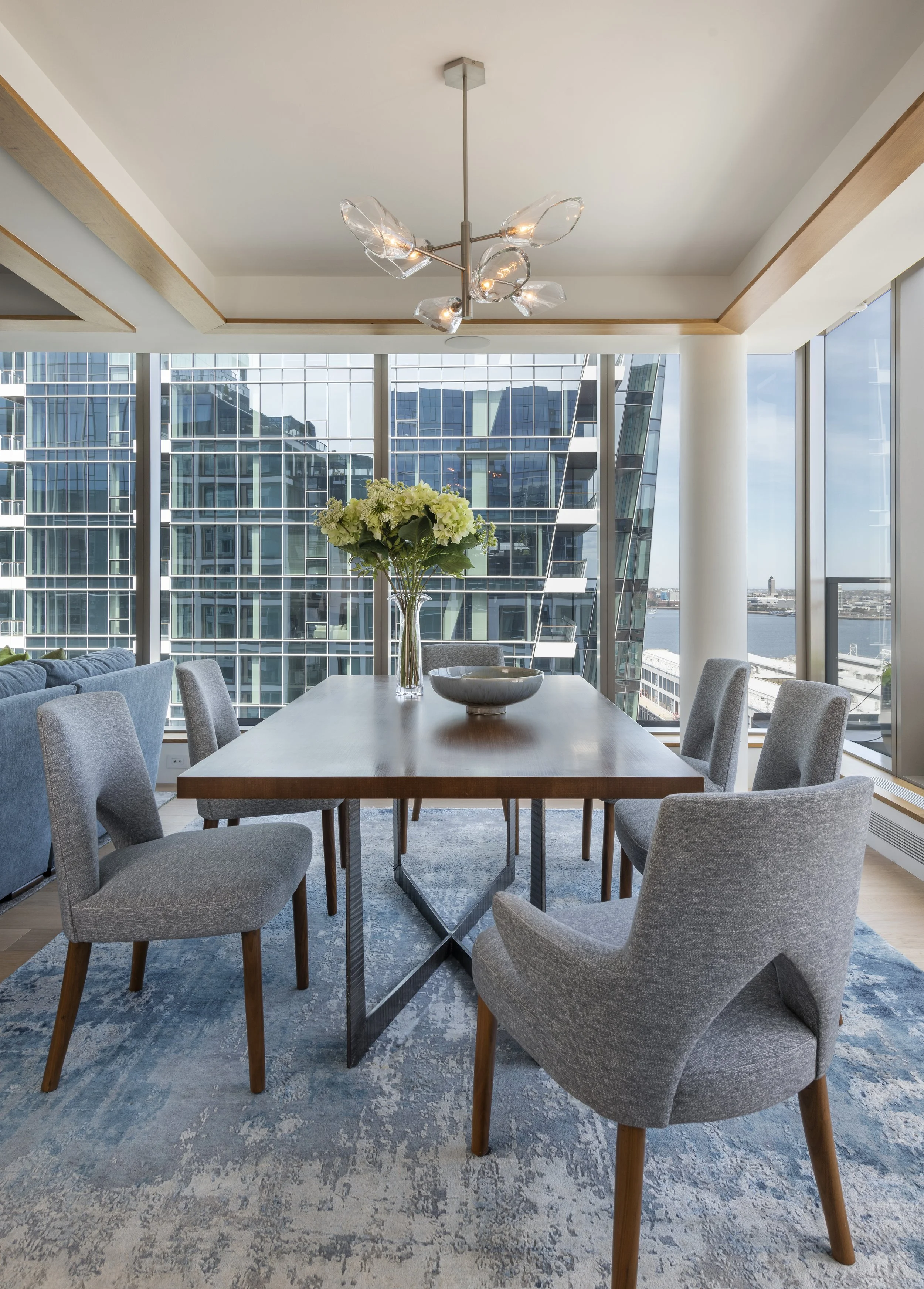 Seaport modern dining room with custom rift-oak table, architectural gray chairs, glass chandelier, silk rug, and harbor views.