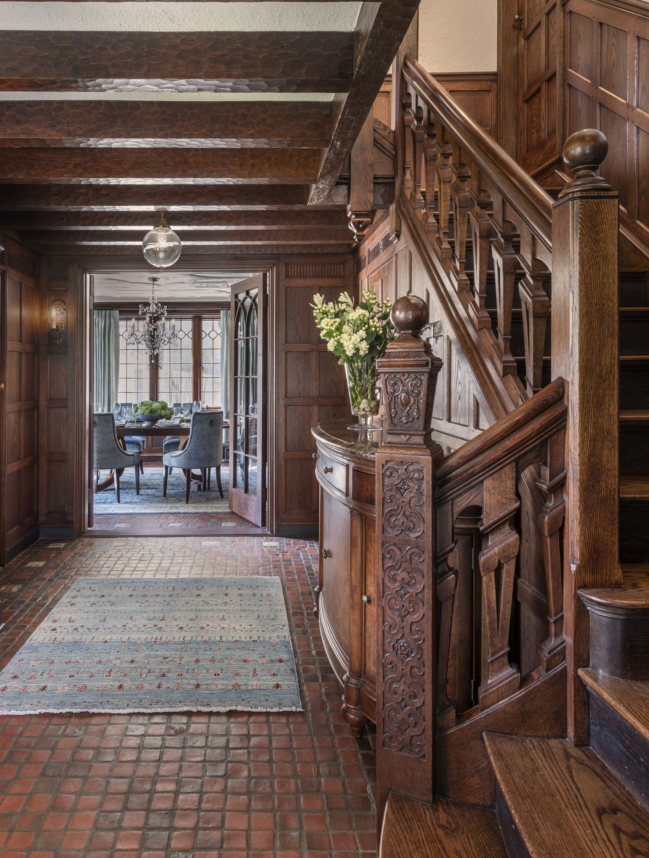 Tudor stair hall with carved oak staircase, terracotta tile floor, modern runner rug, and view to dining room.