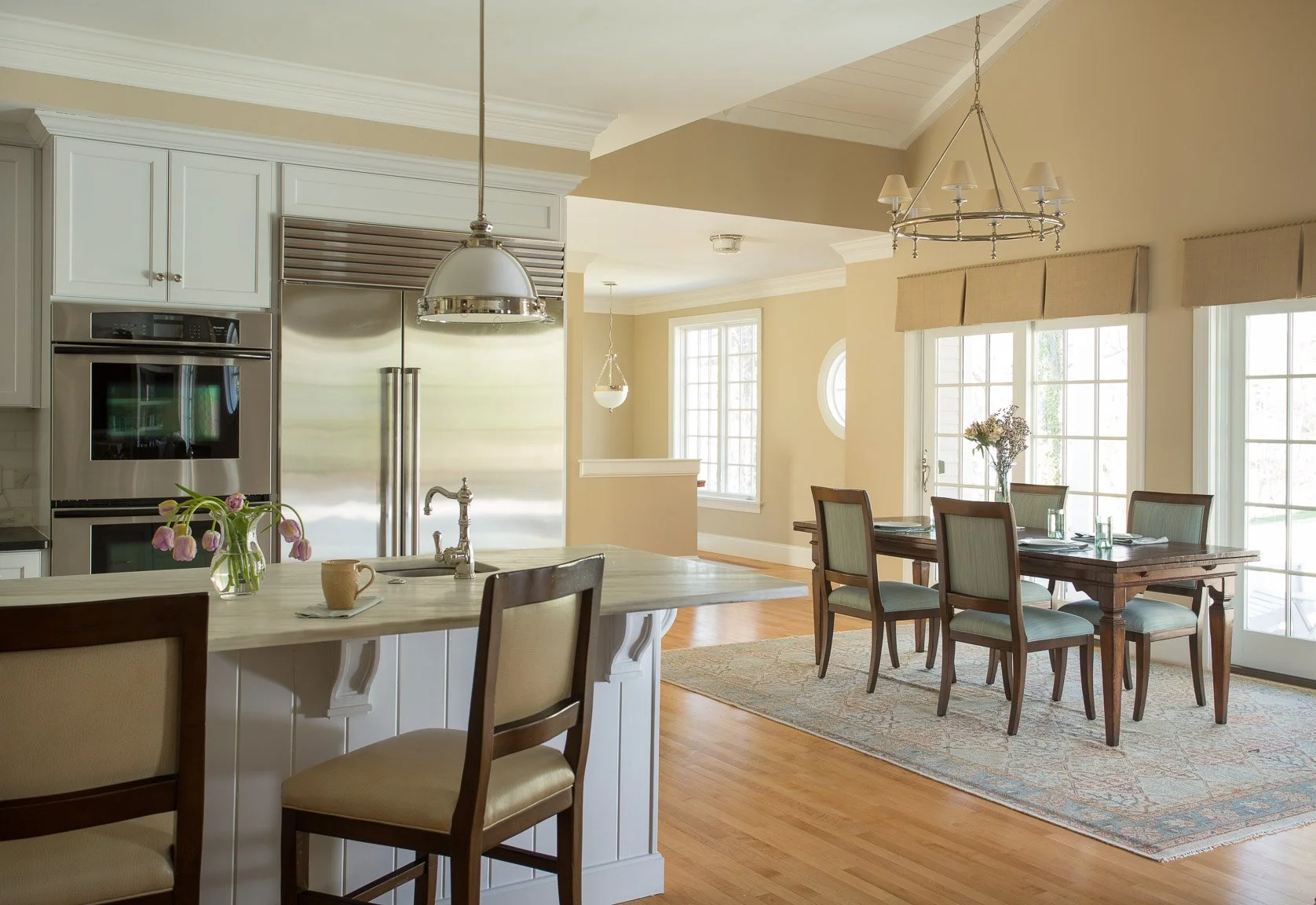 Bright kitchen and dining area with large windows, wooden floor, white cabinetry, and a wooden dining table with six chairs.